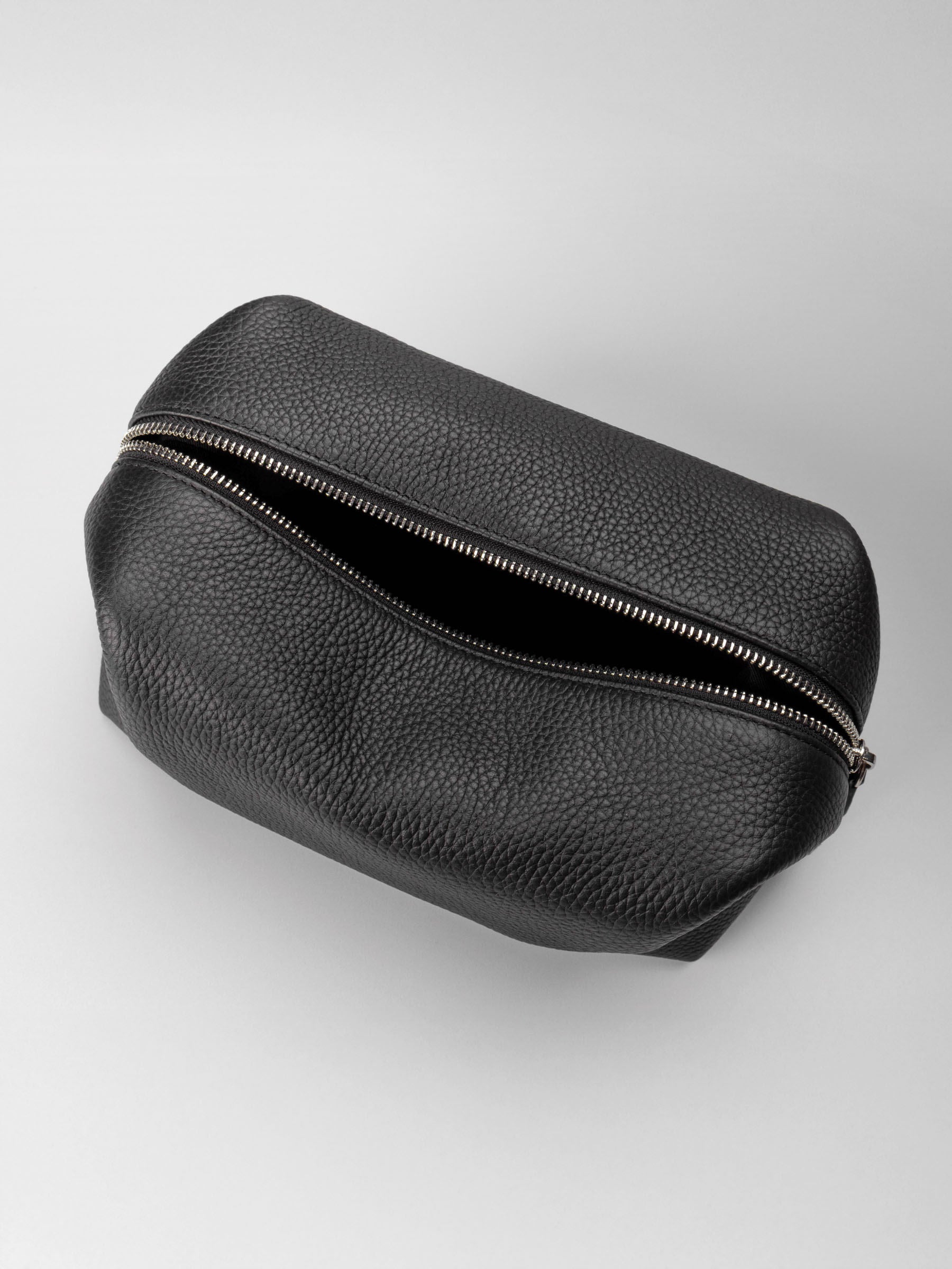 Folded Form Pouch in black pebbled leather, top-down view, unsnapped and open showing silver zipper partially unzipped