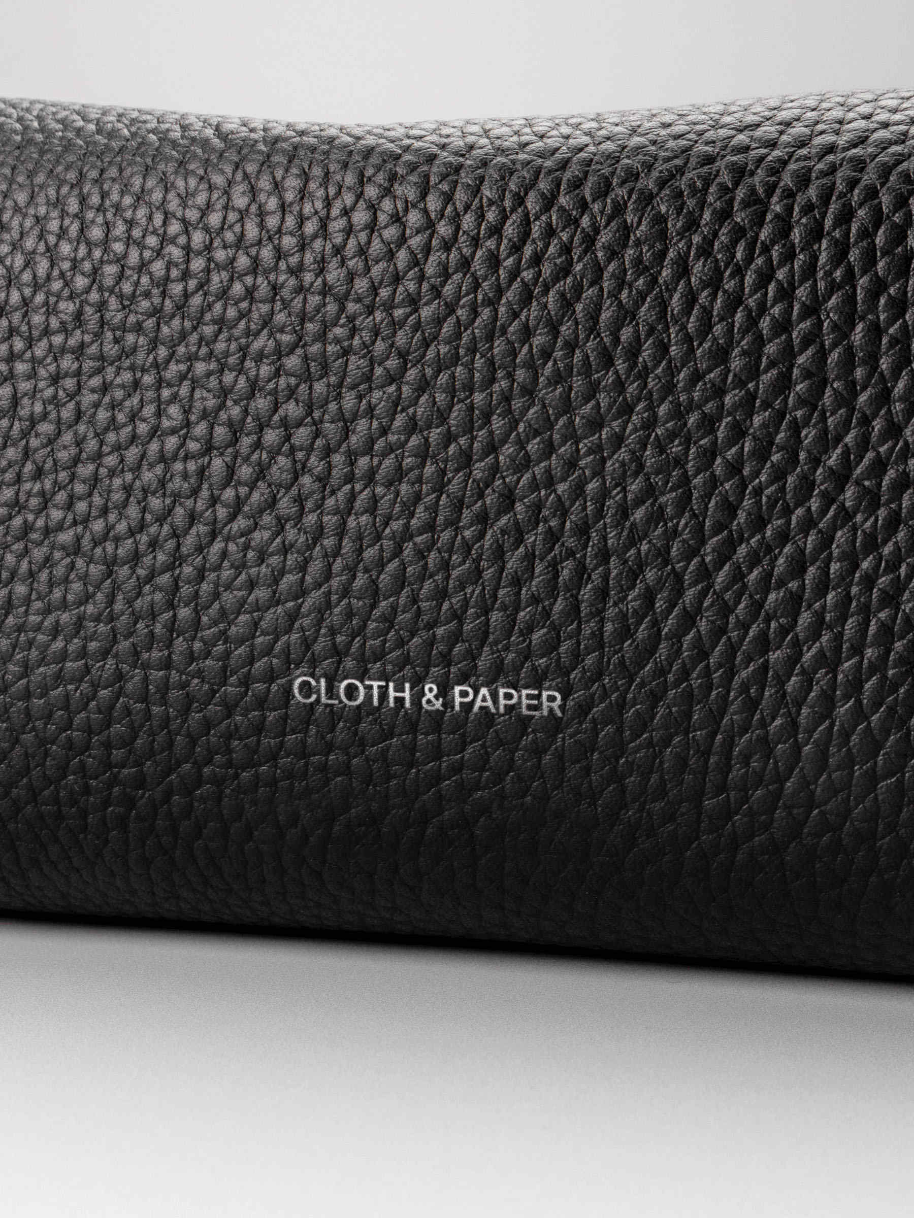 Folded Form Pouch close-up of black pebbled leather texture and silver foil Cloth & Paper logo on exterior