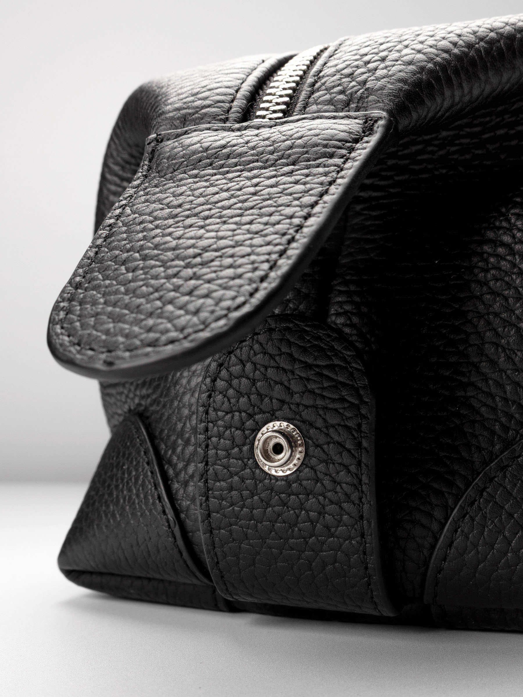 Folded Form Pouch close-up of silver snap hardware on side panel with leather zipper pull and silver zipper visible above