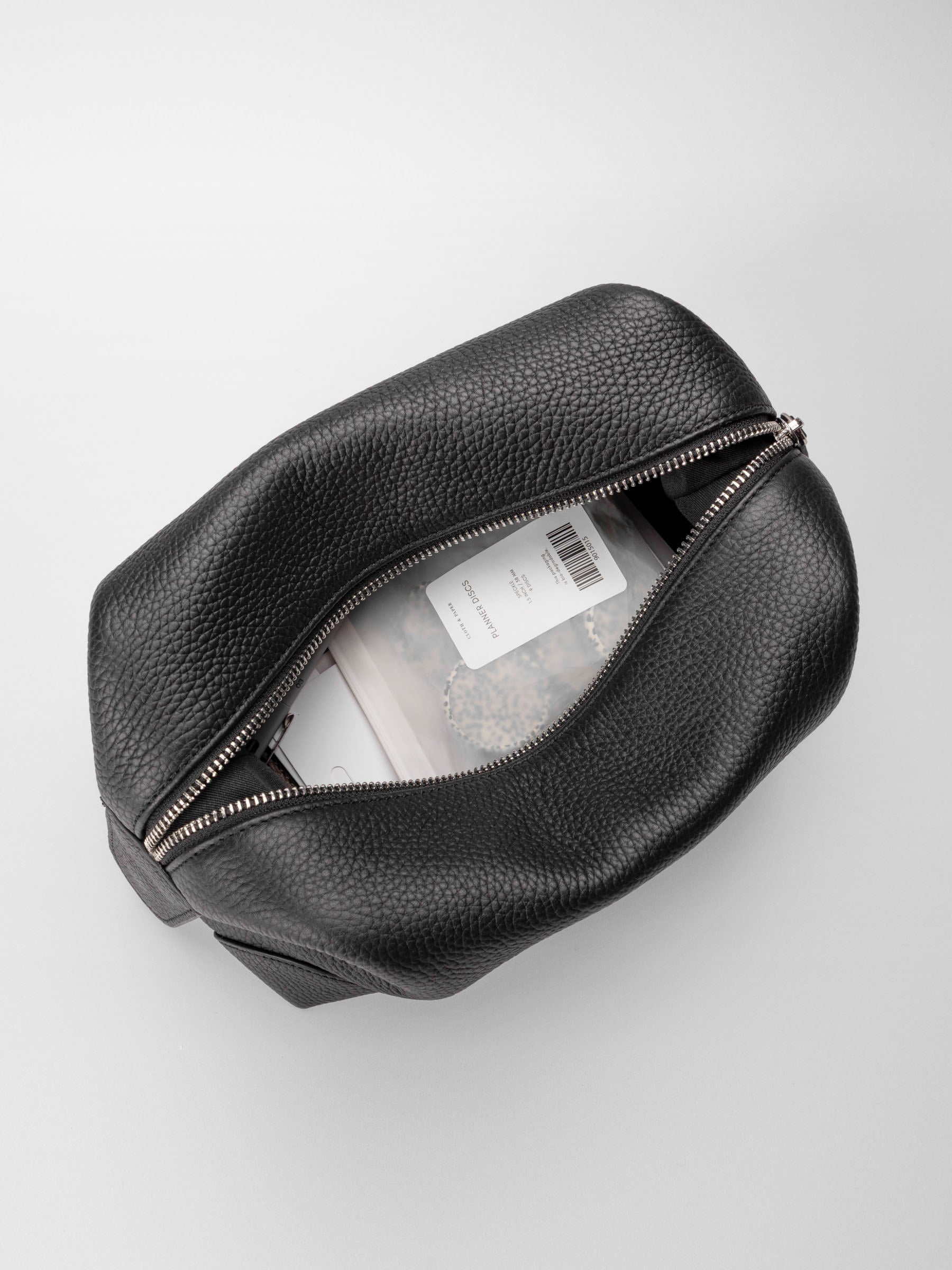 Folded Form Pouch in black pebbled leather, top-down view, open and filled with planner accessories including a package of planner discs
