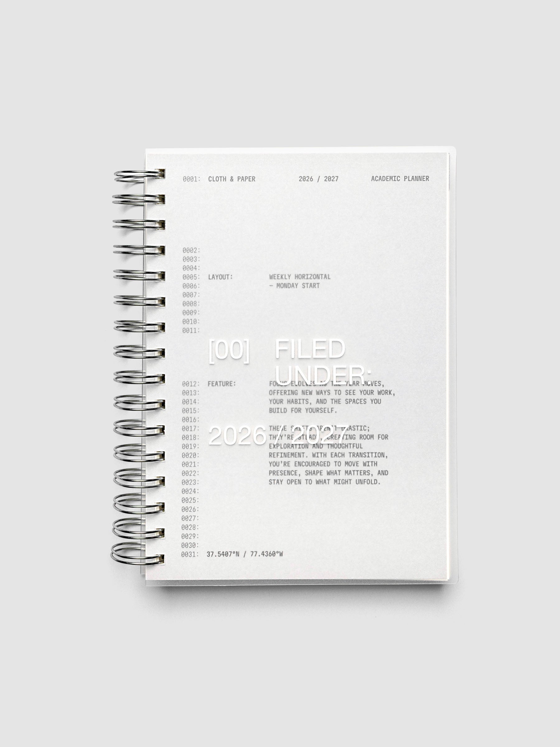 Transparent spiral-bound academic planner closed, showing the grey cardstock dashboard through the clear plastic cover, with silver spiral binding along the left edge
