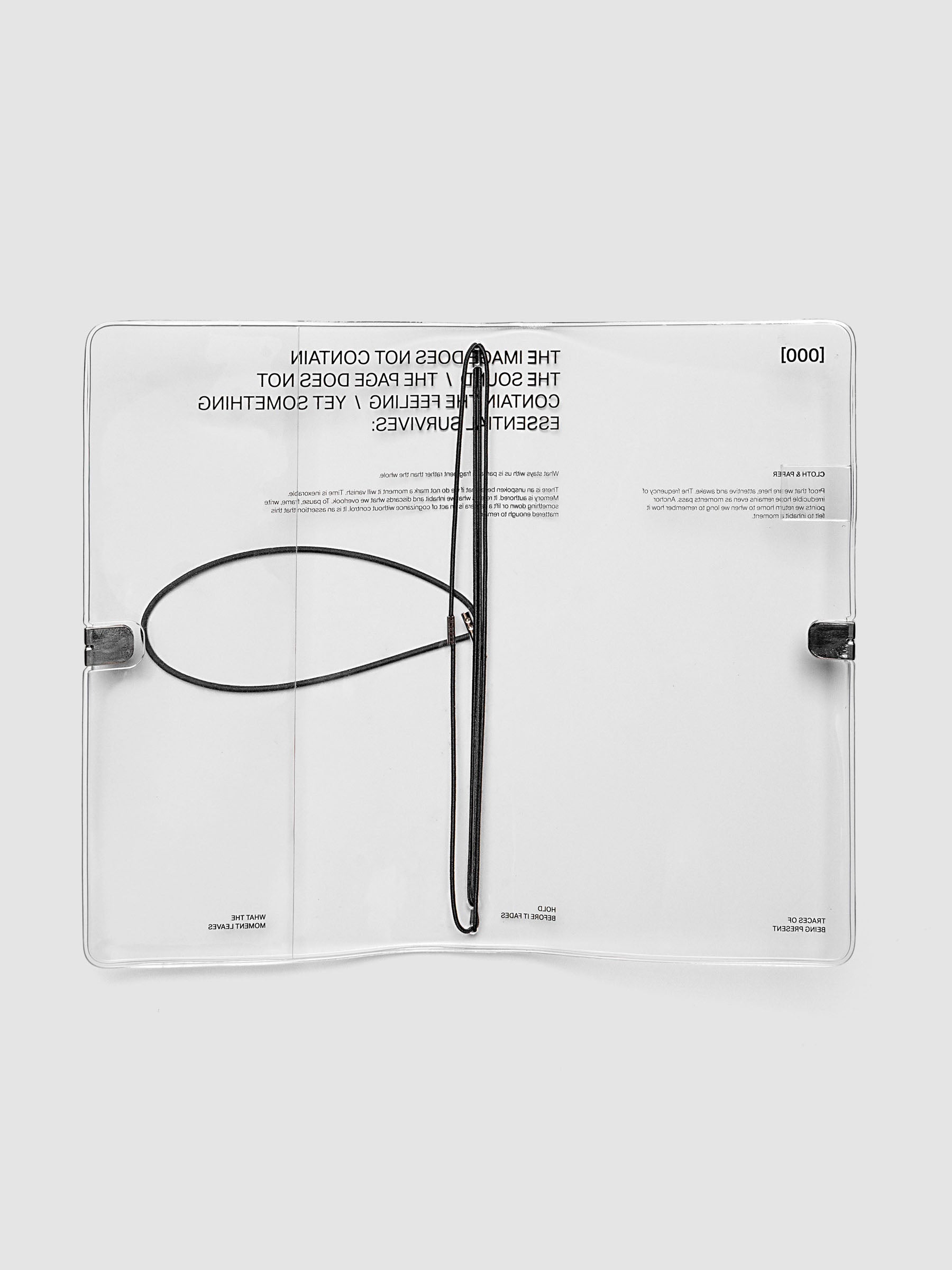What Lasts Travel Notebook Cover in clear vinyl, A5 Slim, open flat lay showing interior with black bungee cord loop and silver metal closures at both sides, typographic text visible across both panels