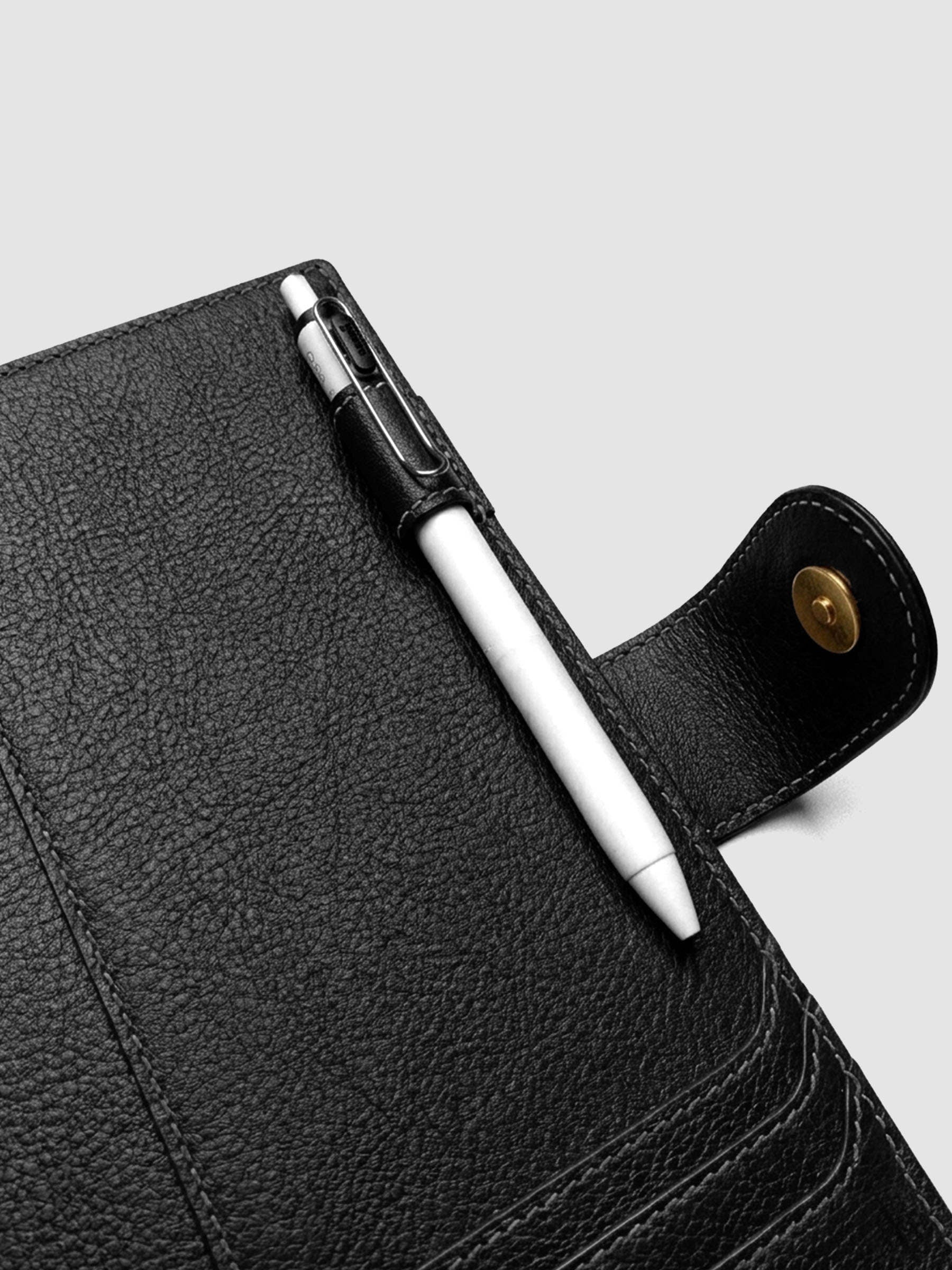 Detail of a pen threaded through the pen loop on the right interior of a black genuine leather A5 planner cover
