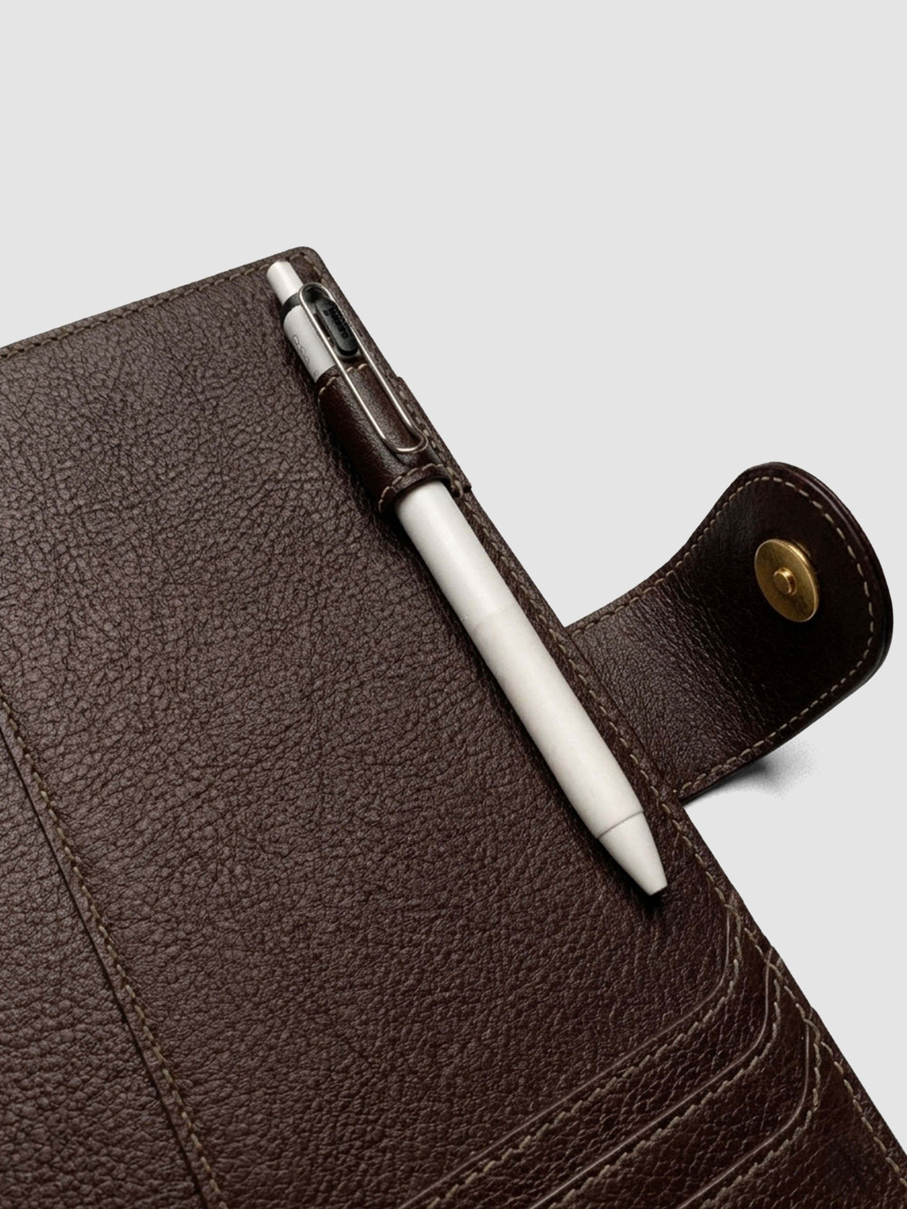 Detail of a pen threaded through the pen loop on the right interior of a dark brown genuine leather A5 planner cover