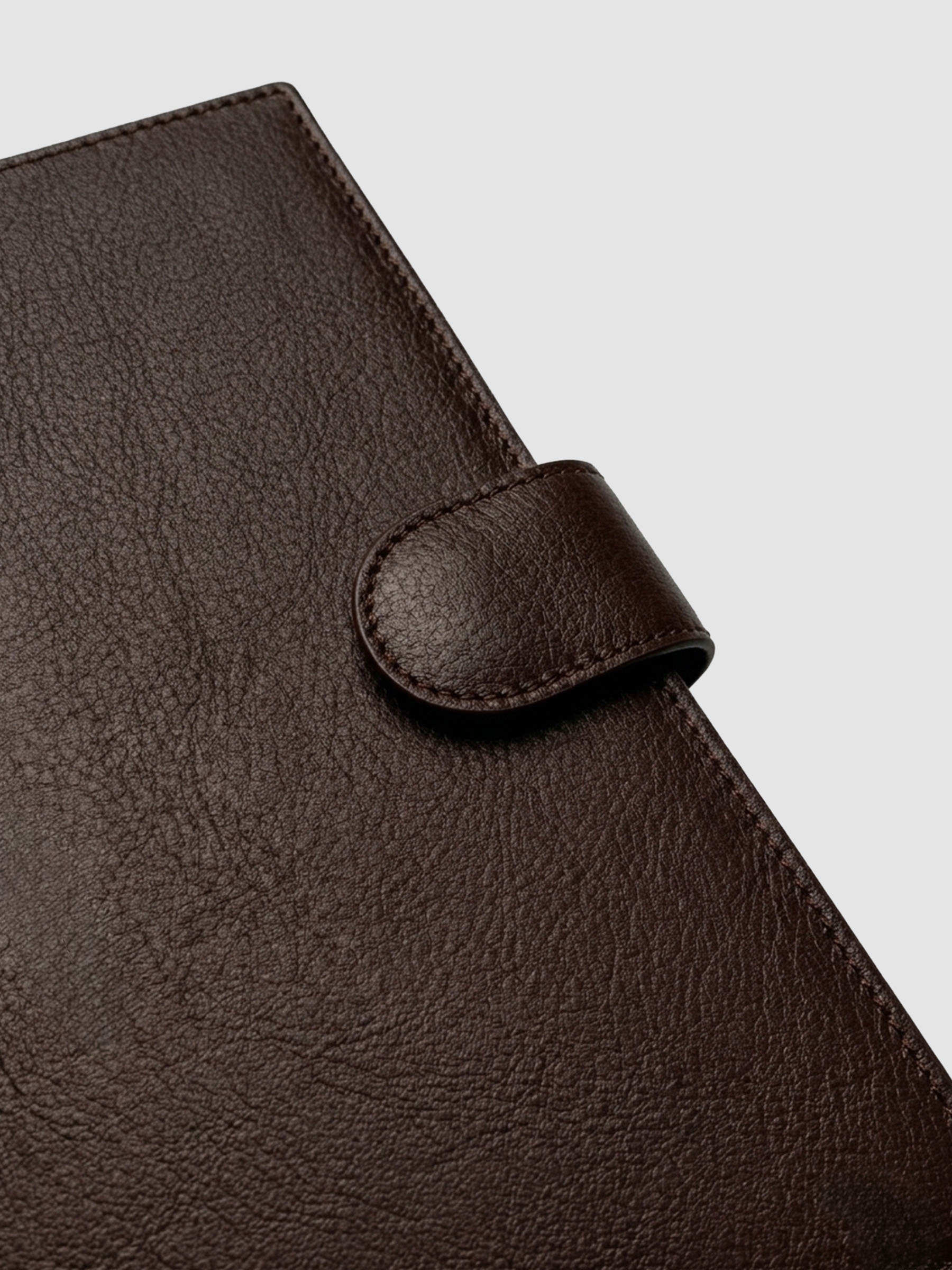 Detail of gold magnetic snap closure securing a dark brown genuine leather A5 planner cover shut