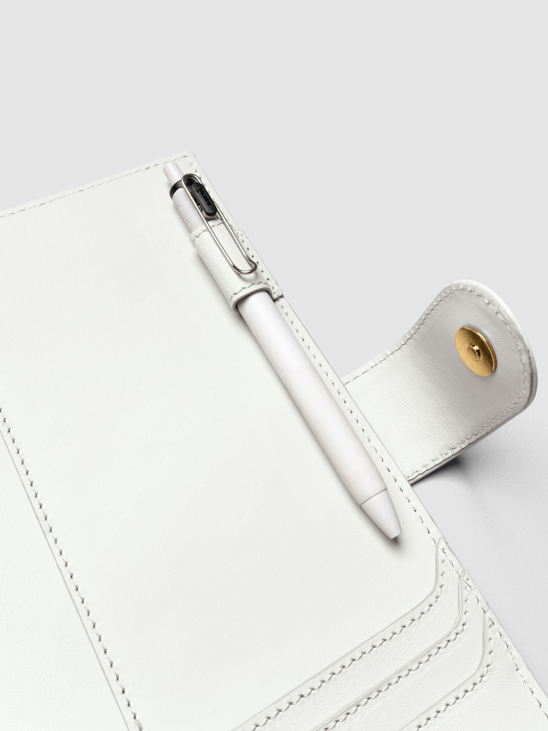 Detail of a pen threaded through the pen loop on the right interior of an off-white genuine leather A5 planner cover