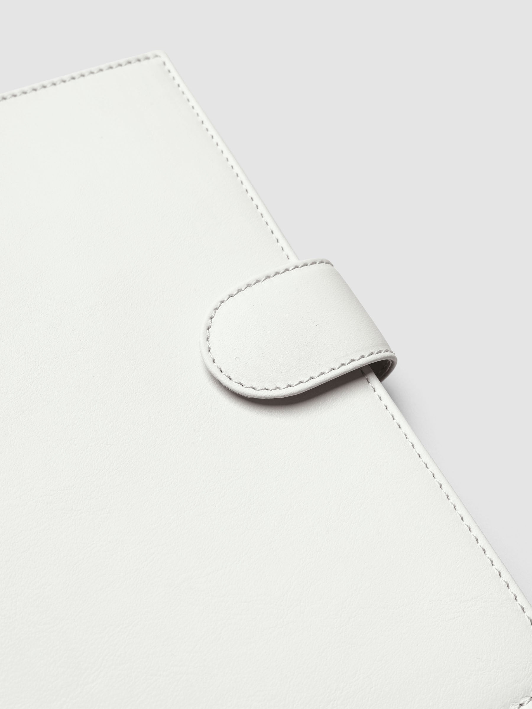 Detail of gold magnetic snap closure securing an off-white genuine leather A5 planner cover shut