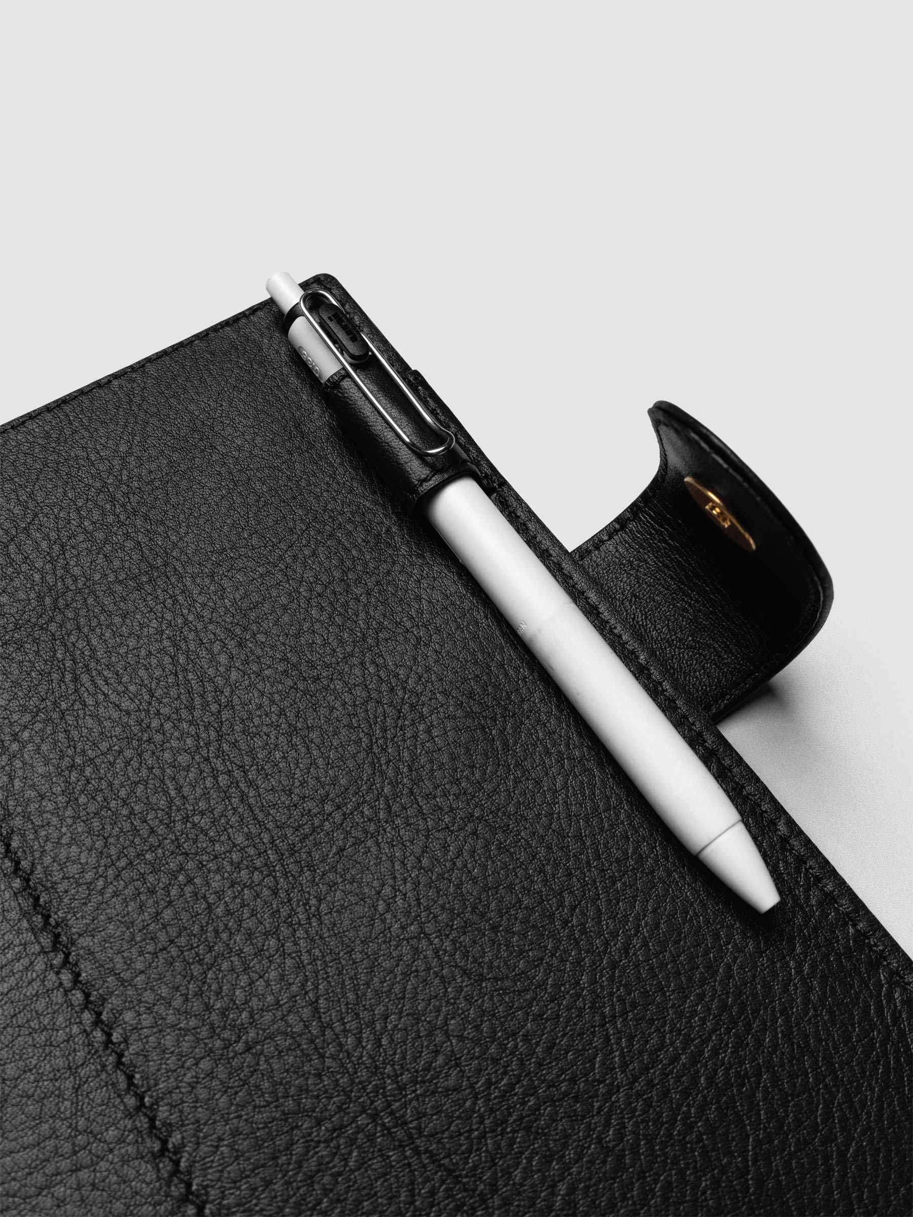 Detail of a pen threaded through the pen loop on the right interior of a black genuine leather Personal Wide 6-ring planner cover