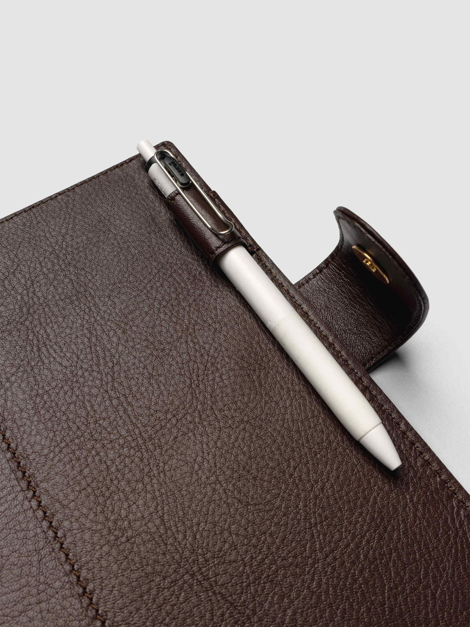 Detail of a pen threaded through the pen loop on the right interior of a dark brown genuine leather Personal Wide 6-ring planner cover