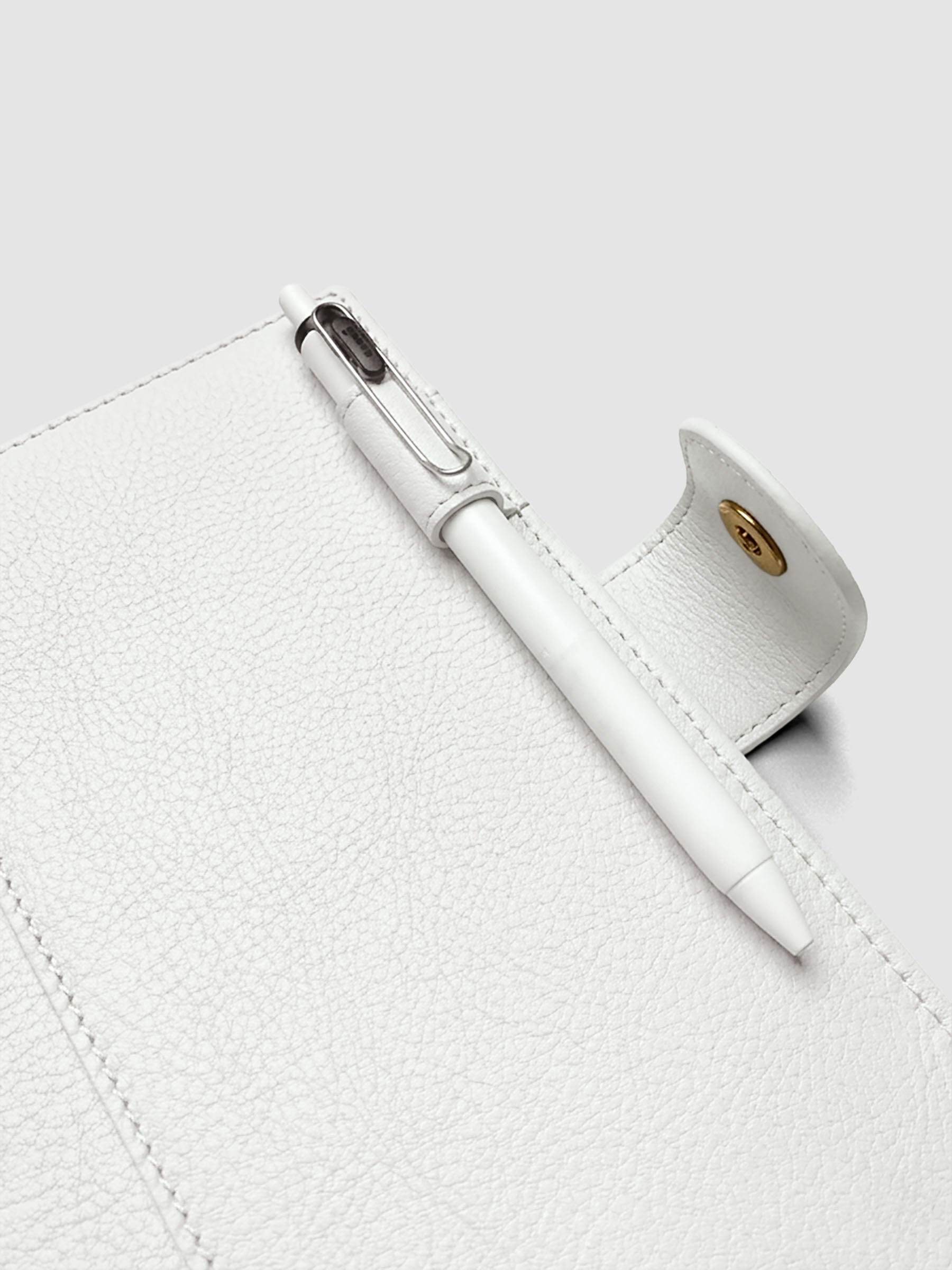 Detail of a pen threaded through the pen loop on the right interior of an off-white genuine leather Personal Wide 6-ring planner cover