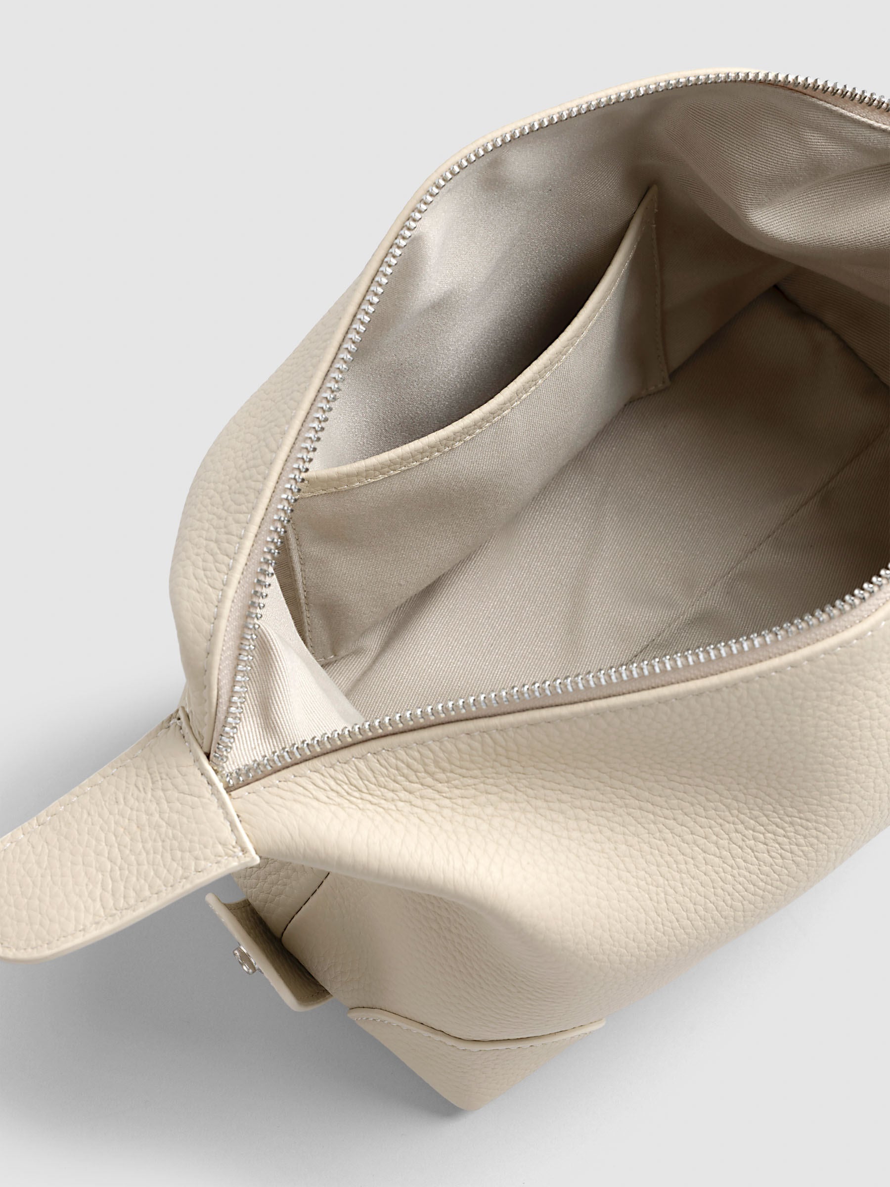 Folded Form Pouch in warm beige pebbled leather, angled interior view showing taupe fabric lining and open side pocket with silver zipper