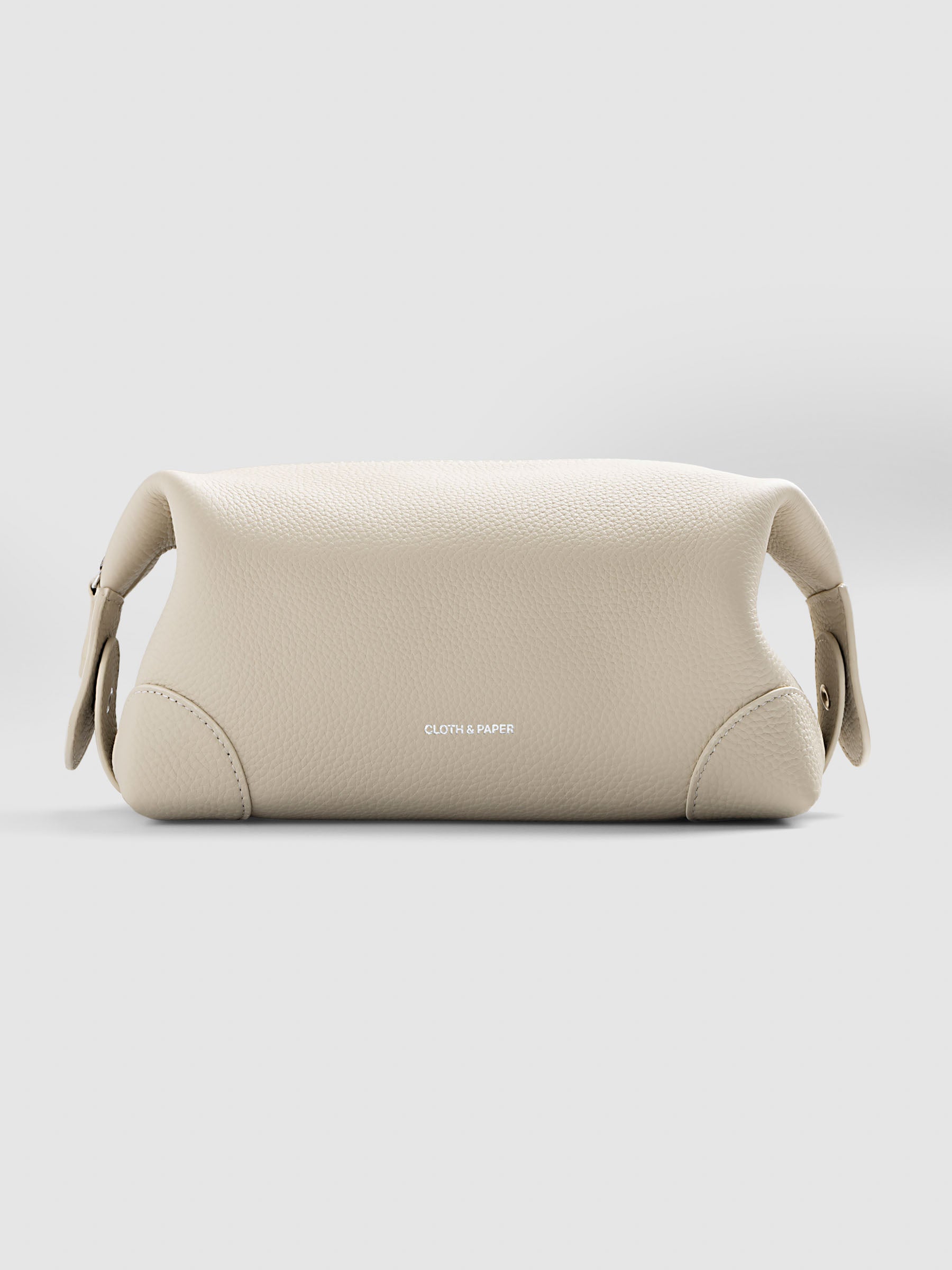 Folded Form Pouch in warm beige pebbled leather, three-quarter view, snapped closed with silver foil Cloth & Paper logo visible on exterior