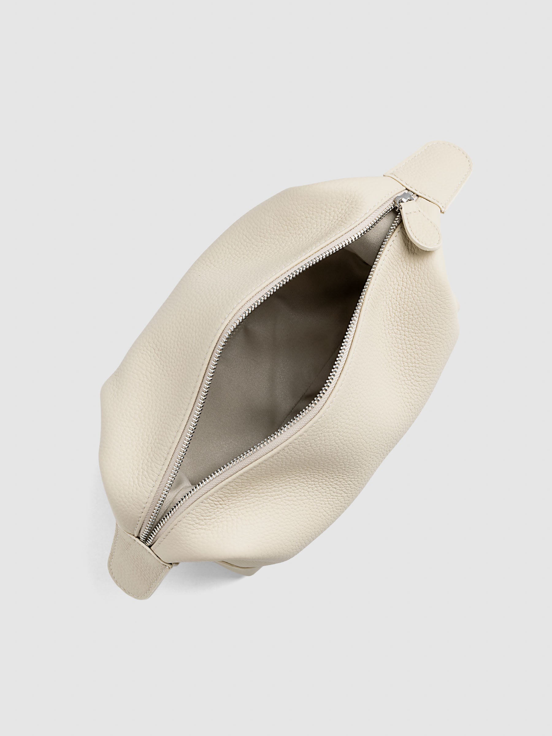 Folded Form Pouch in warm beige pebbled leather, top-down view, unsnapped and open with silver zipper partially unzipped and taupe fabric lining visible