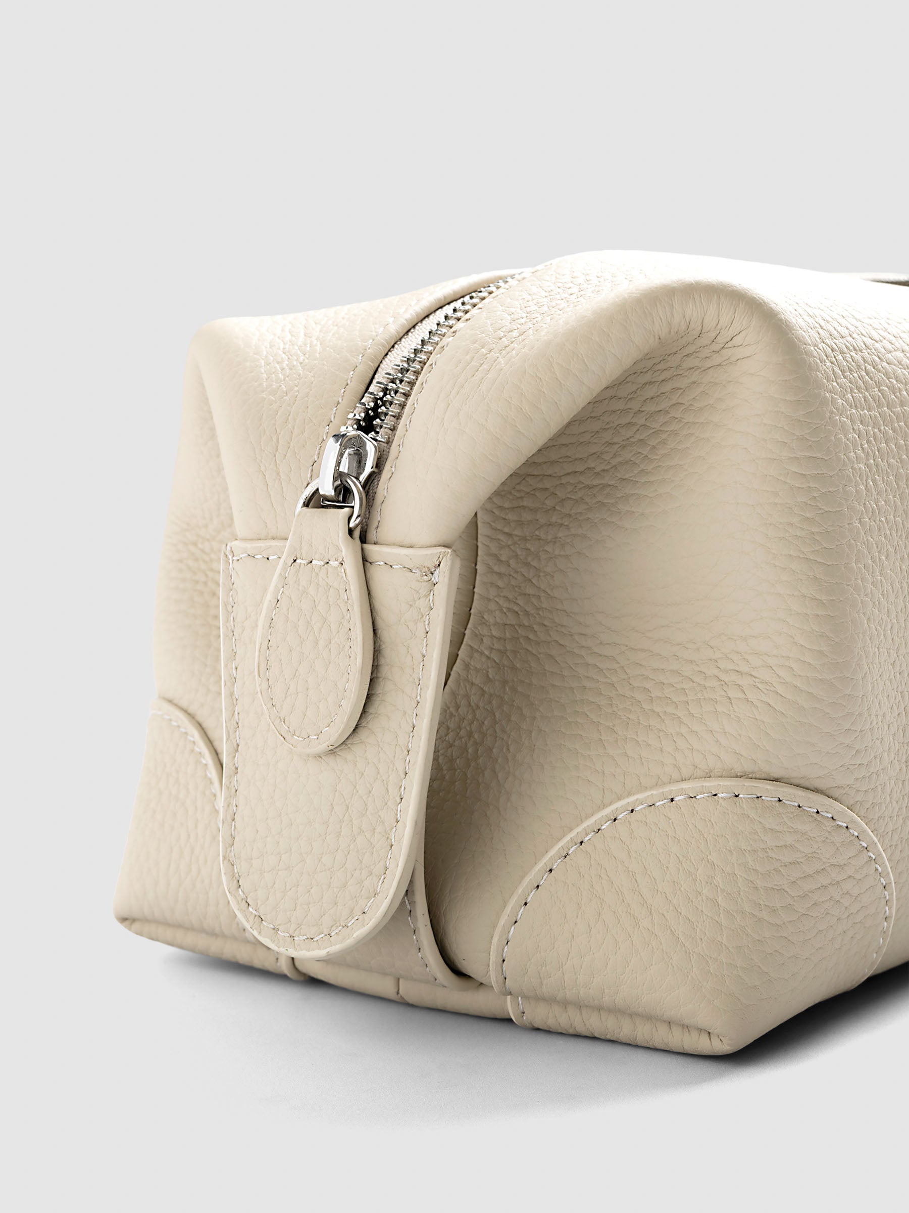 Folded Form Pouch in warm beige pebbled leather, side view showing silver zipper, leather zipper pull, and rounded corner stitching detail