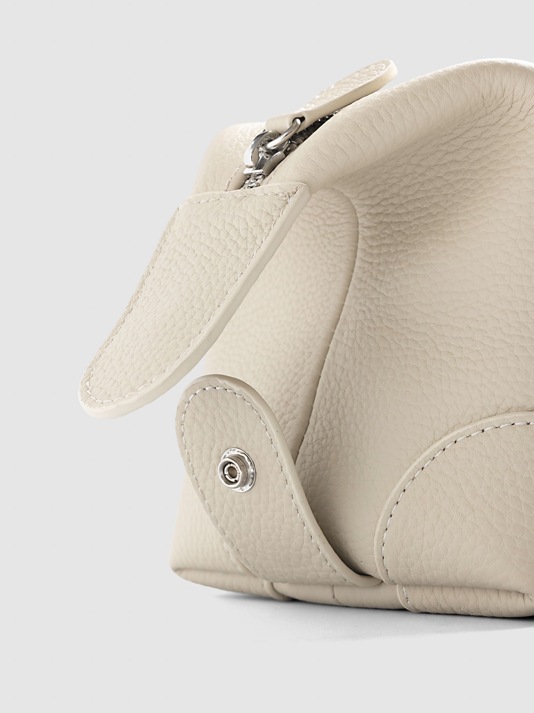 Folded Form Pouch in warm beige pebbled leather, close-up of silver snap hardware on side panel with leather zipper pull and silver zipper visible above