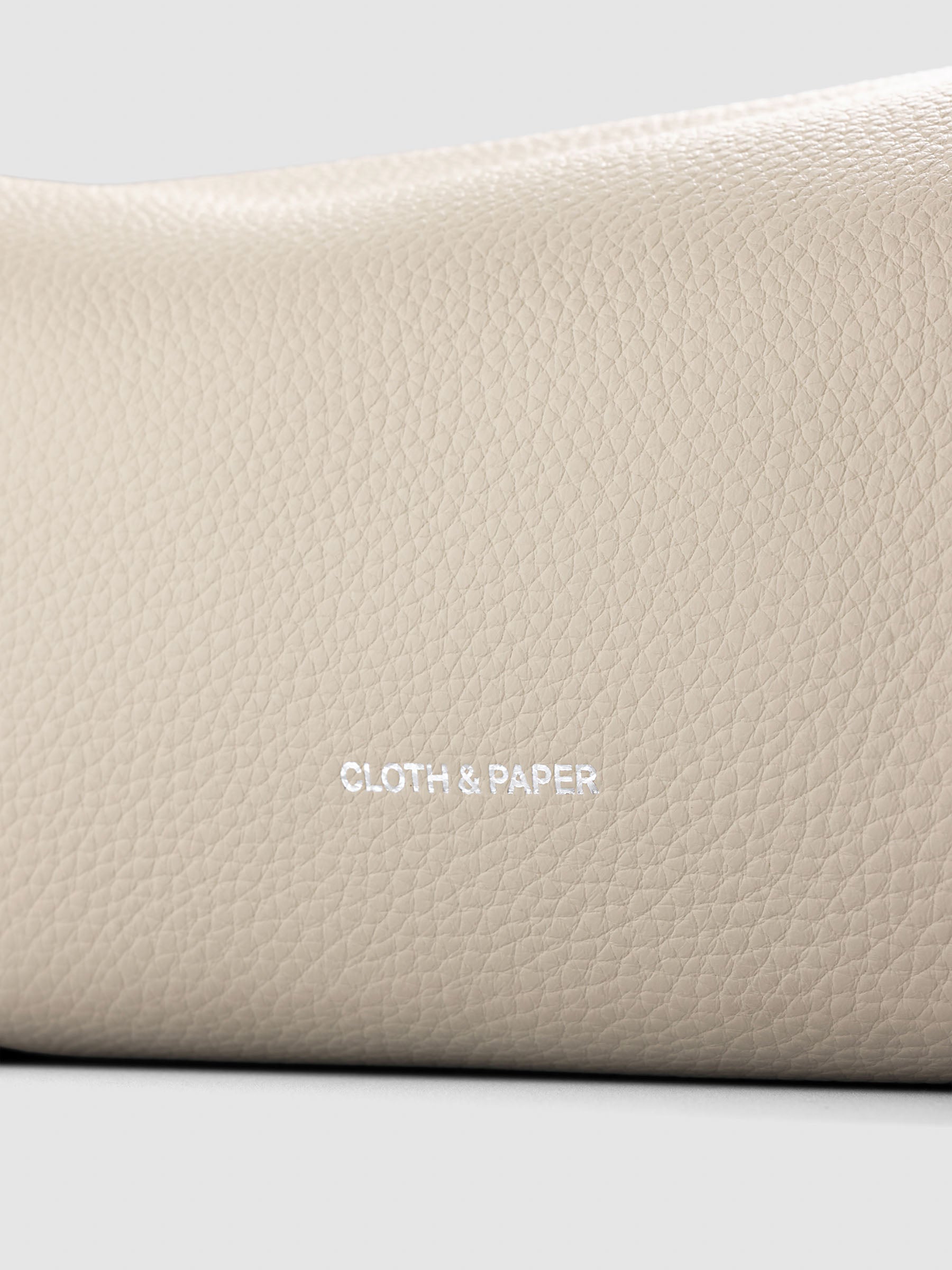 Folded Form Pouch close-up of warm beige pebbled leather texture and silver foil Cloth & Paper logo on exterior