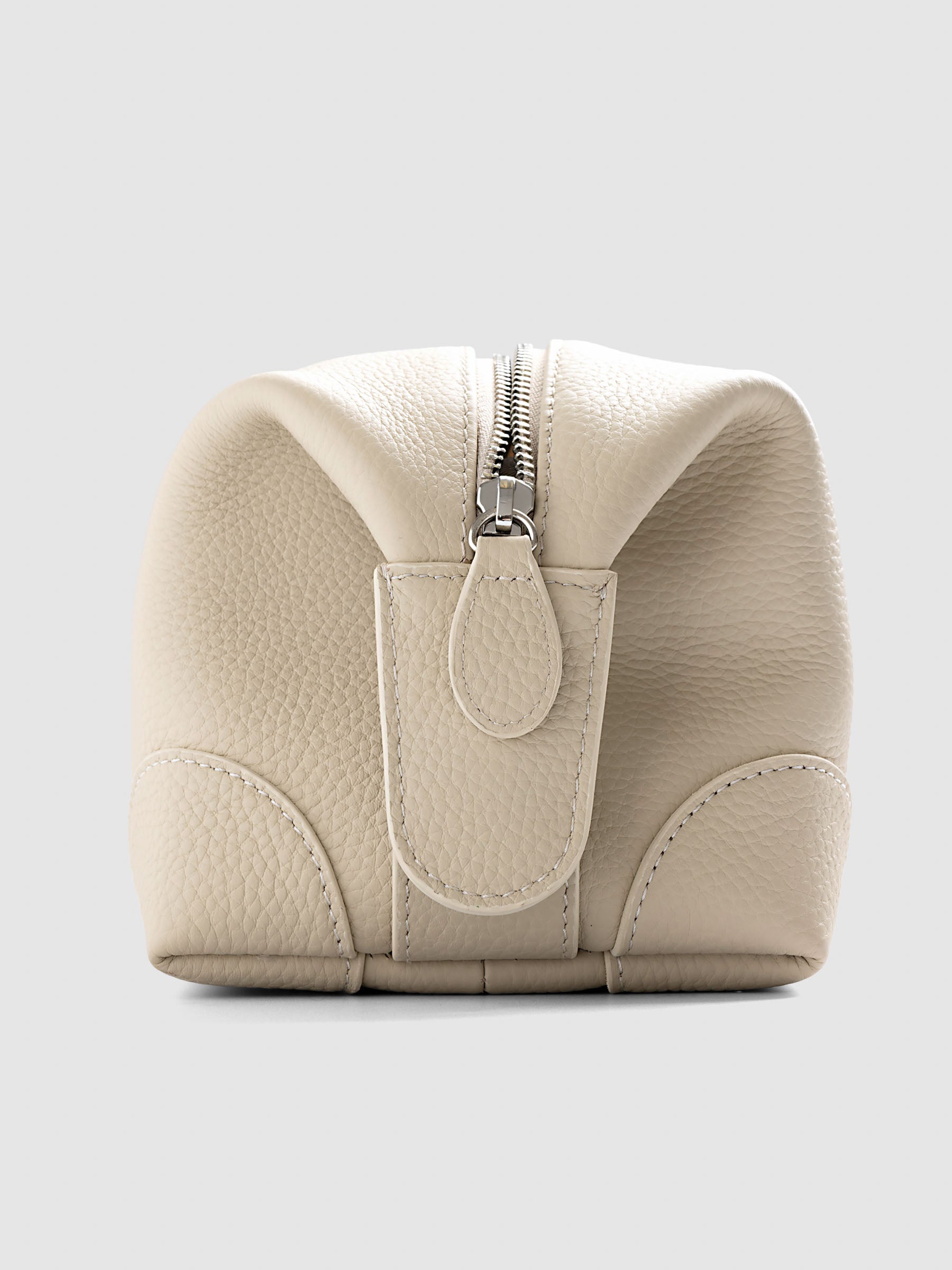 Folded Form Pouch in warm beige pebbled leather, back view showing leather zipper pull, silver zipper, and rounded corner panel detail