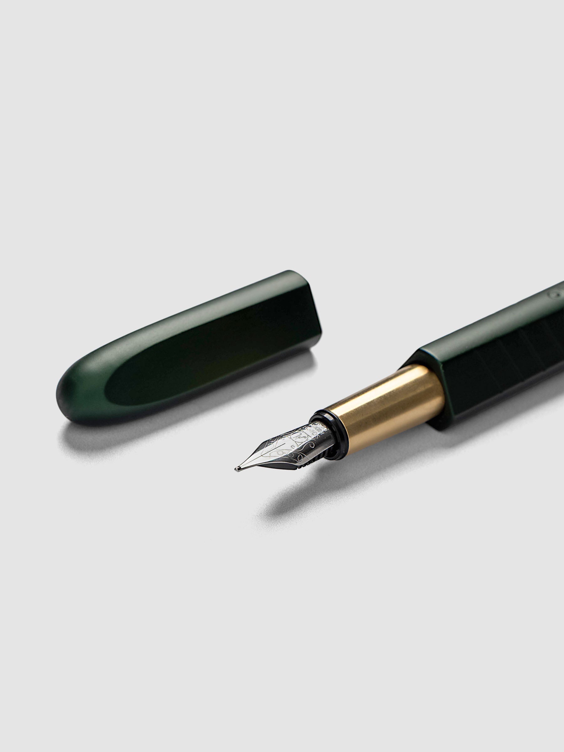 Kolo Tino Fountain Pen in Anodized Aluminum Verdant, a deep forest green barrel with gold accents and silver medium nib shown with cap off, close-up