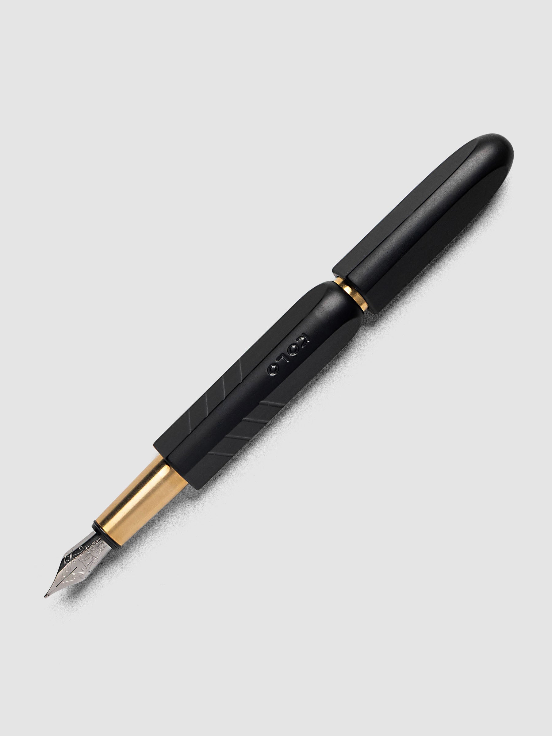 Kolo Tino Fountain Pen in Anodized Aluminum Noir, a matte black barrel with gold accents and silver medium nib shown capped, full pen angled view