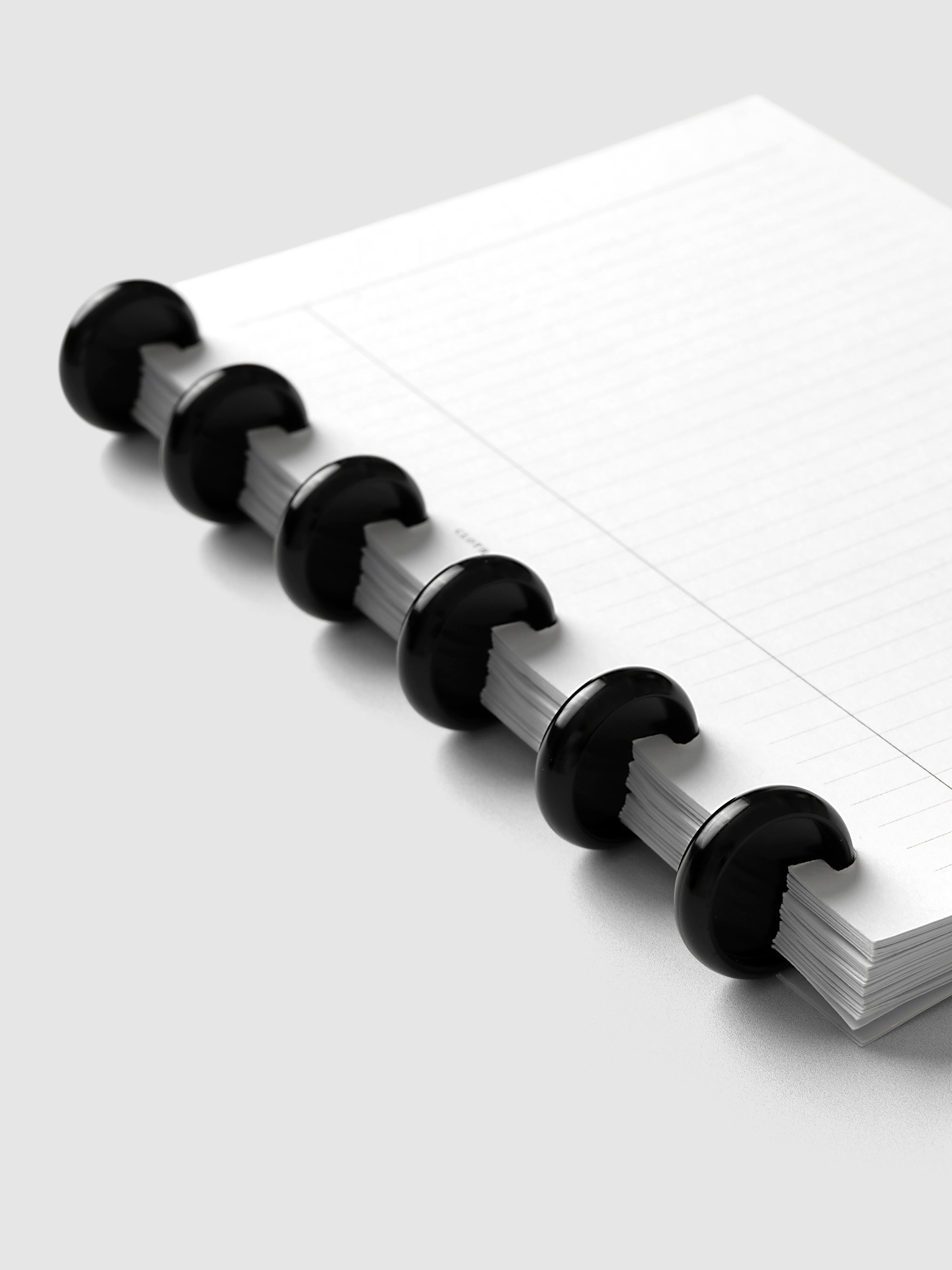Aluminum Planner Discs | Black, 0.75 Inch, installed on a discbound planner with lined paper, close-up of six discs from the side showing a narrower planner profile