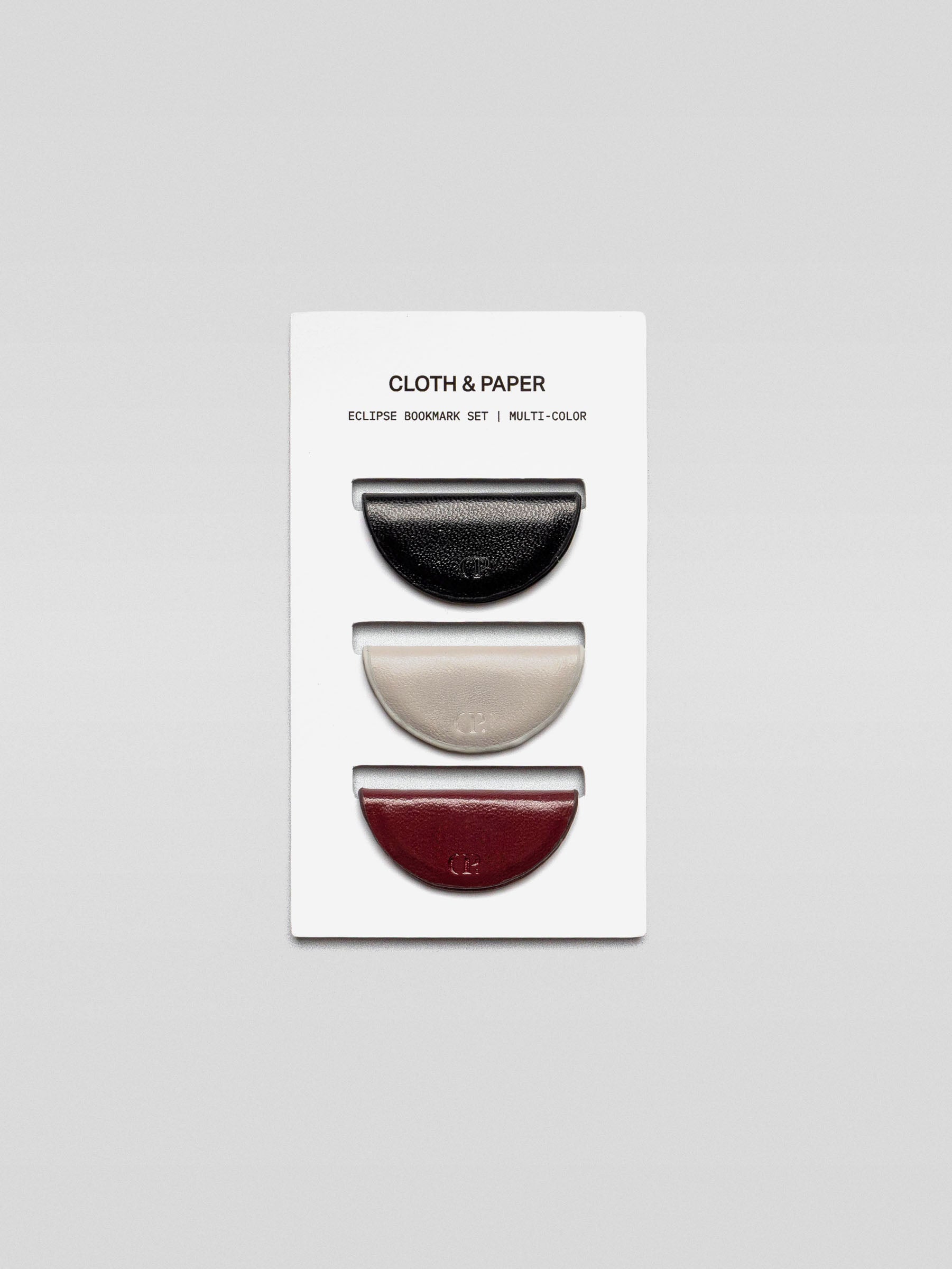 A set of three semi-circle leather magnetic bookmarks in black, cream, and burgundy colors, displayed on a branded Cloth & Paper card.