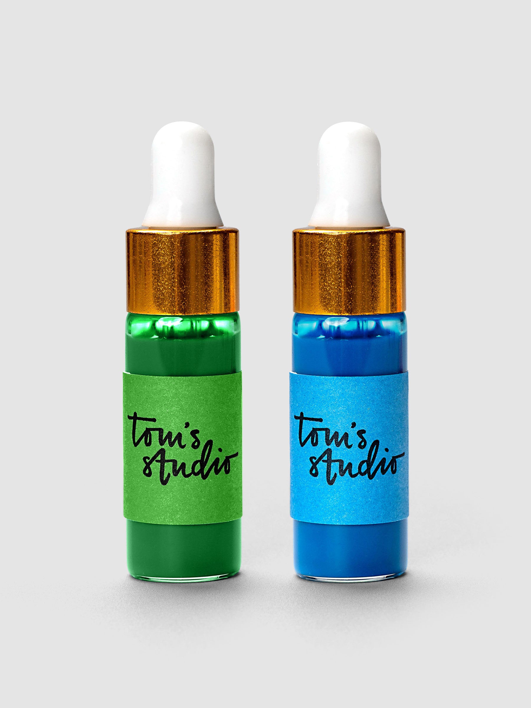Two Tom's Studio ink bottles with gold caps and white droppers in green and blue