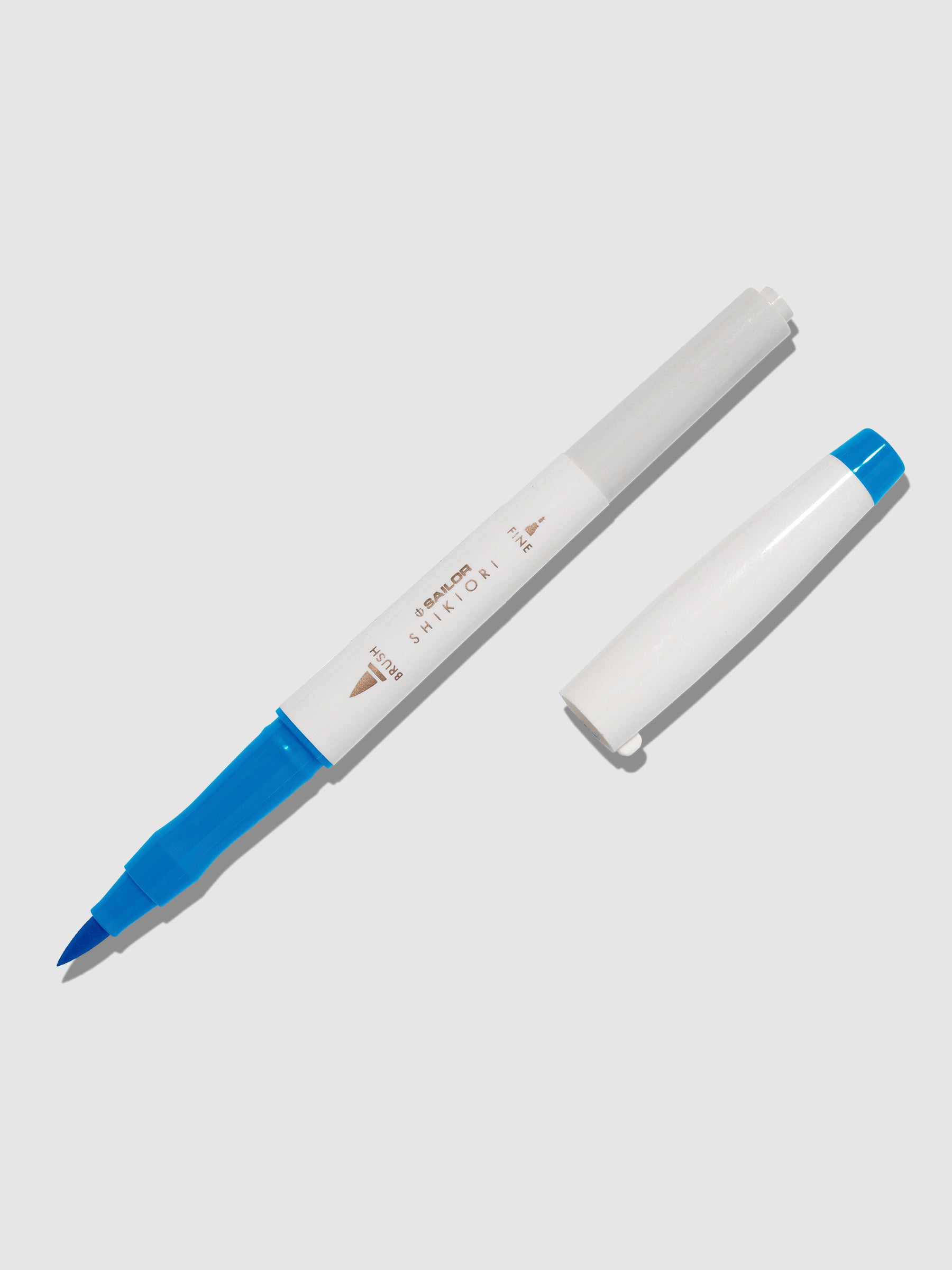 Brush pen displayed on a neutral background. It is uncapped with its brush nib exposed, and the cap lying parallel to the marker. Color pictured is Souten.
