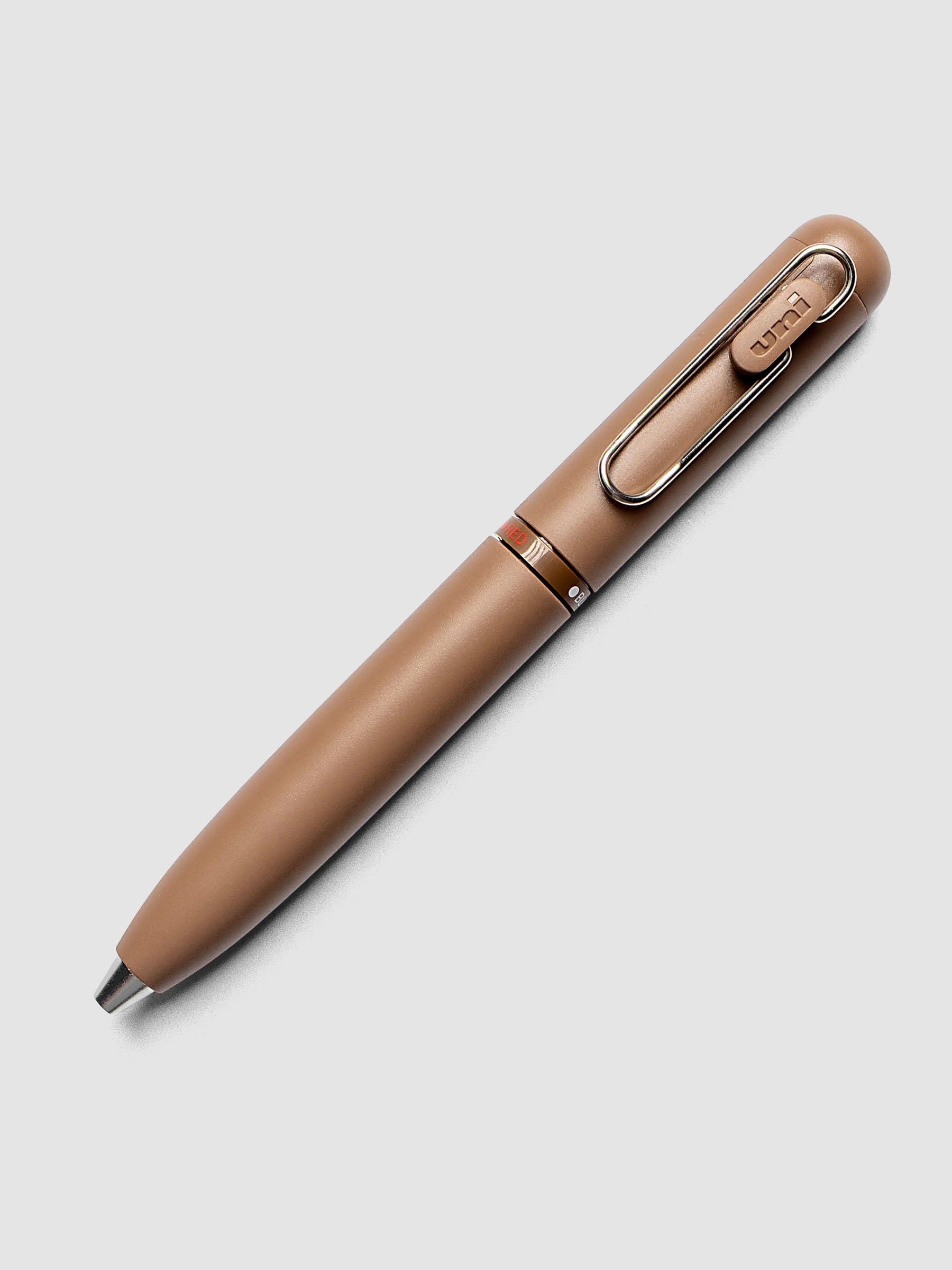 Uni-ball One 3-Color Ballpoint Pen in brown laid diagonally showing clip and RED color indicator