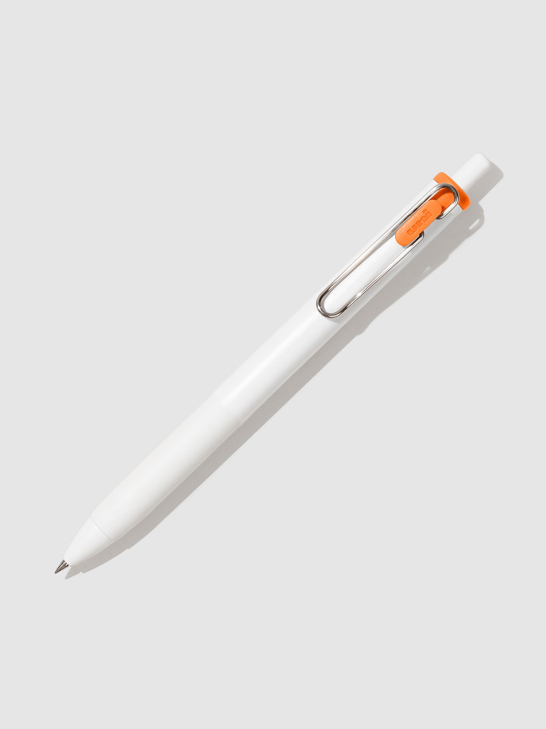 Uni-ball One Gel Pen, Orange, Cloth and Paper. Pen tilted slightly to the right on a neutral background.