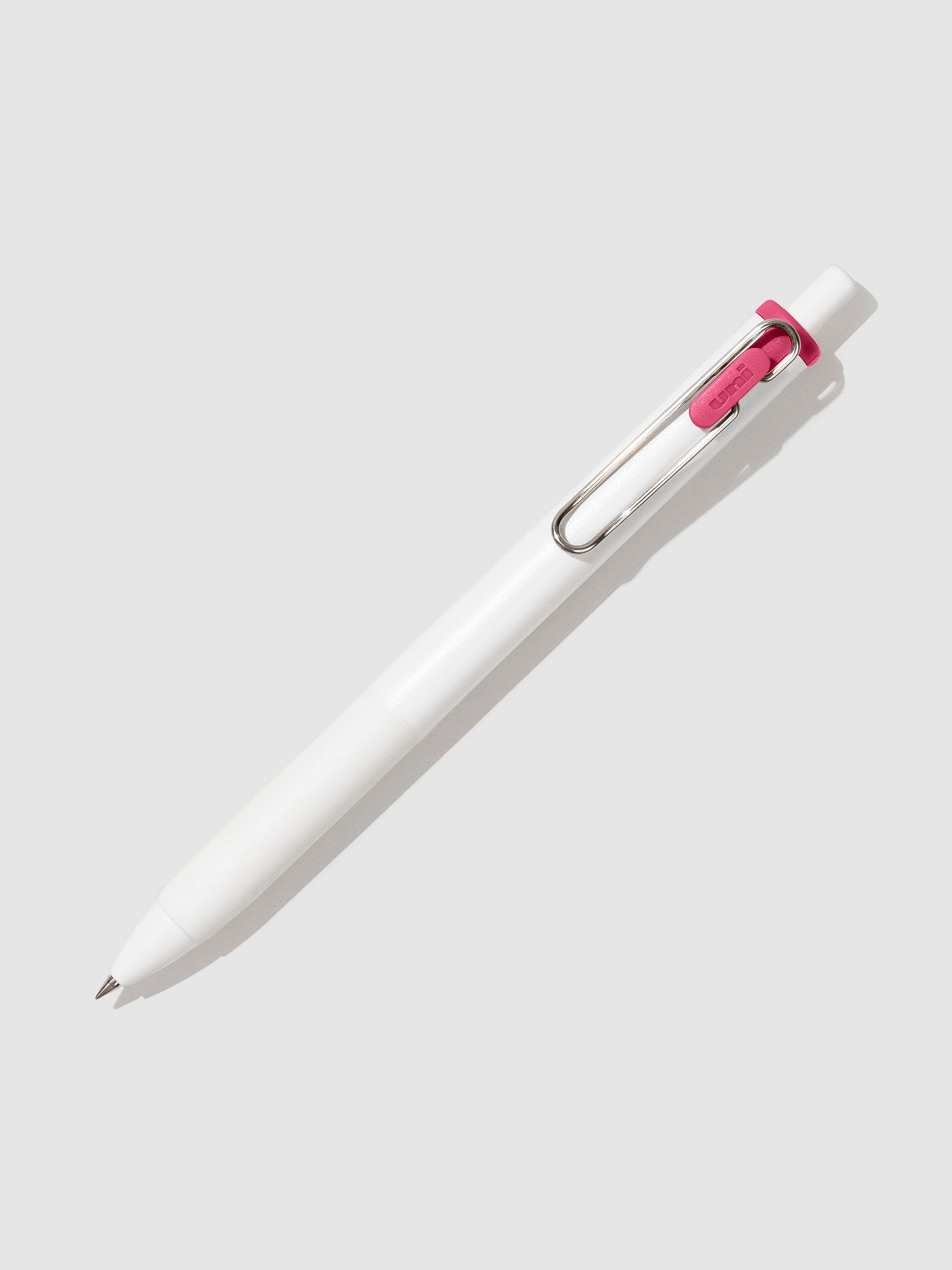 Uni-ball One Gel Pen, Pink, Cloth and Paper. Pen tilted slightly to the right on a neutral background.