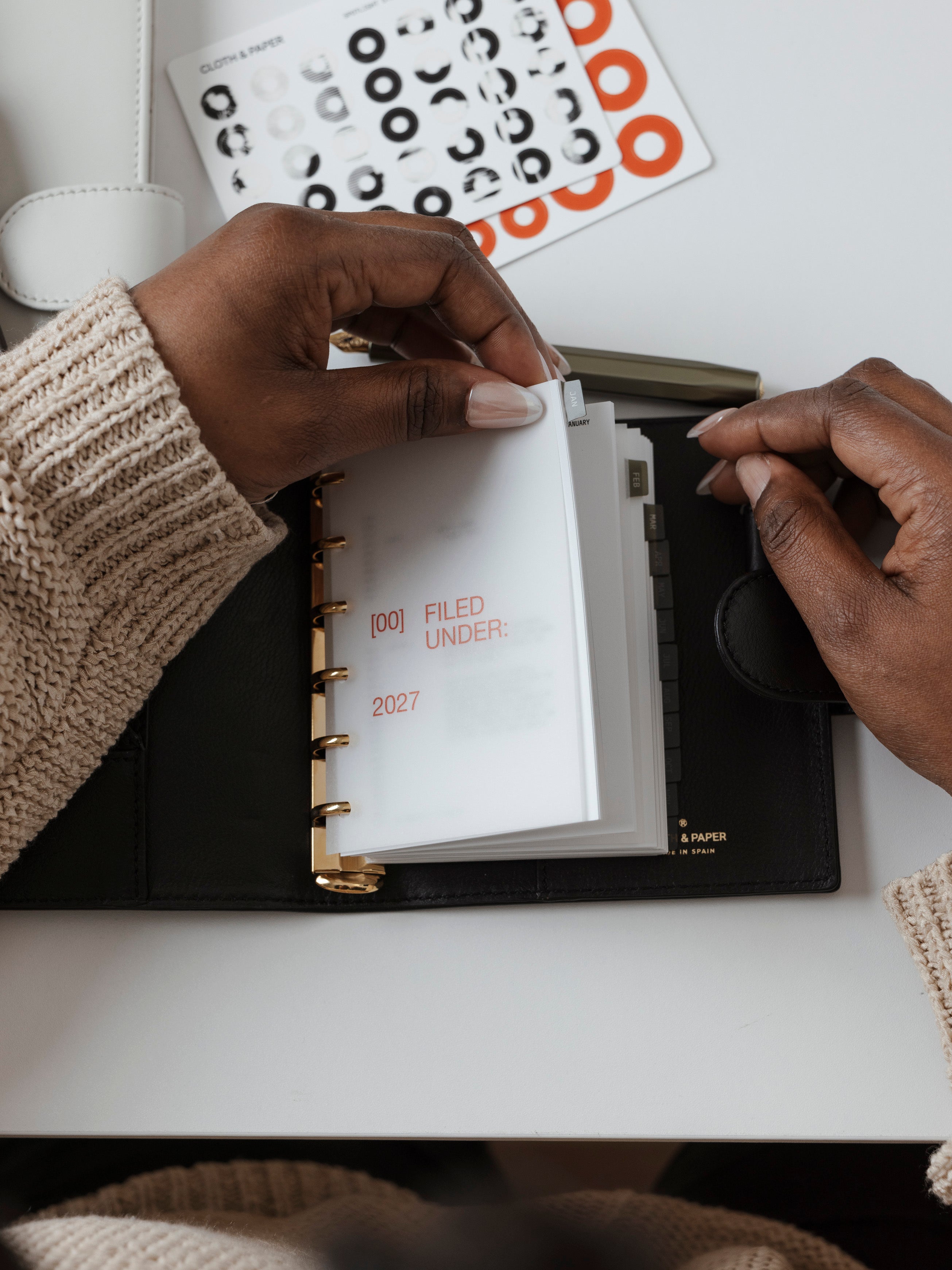 A top-down view of a person flipping through a 6-ring planner with a frosted translucent dashboard in Rouge colored text.