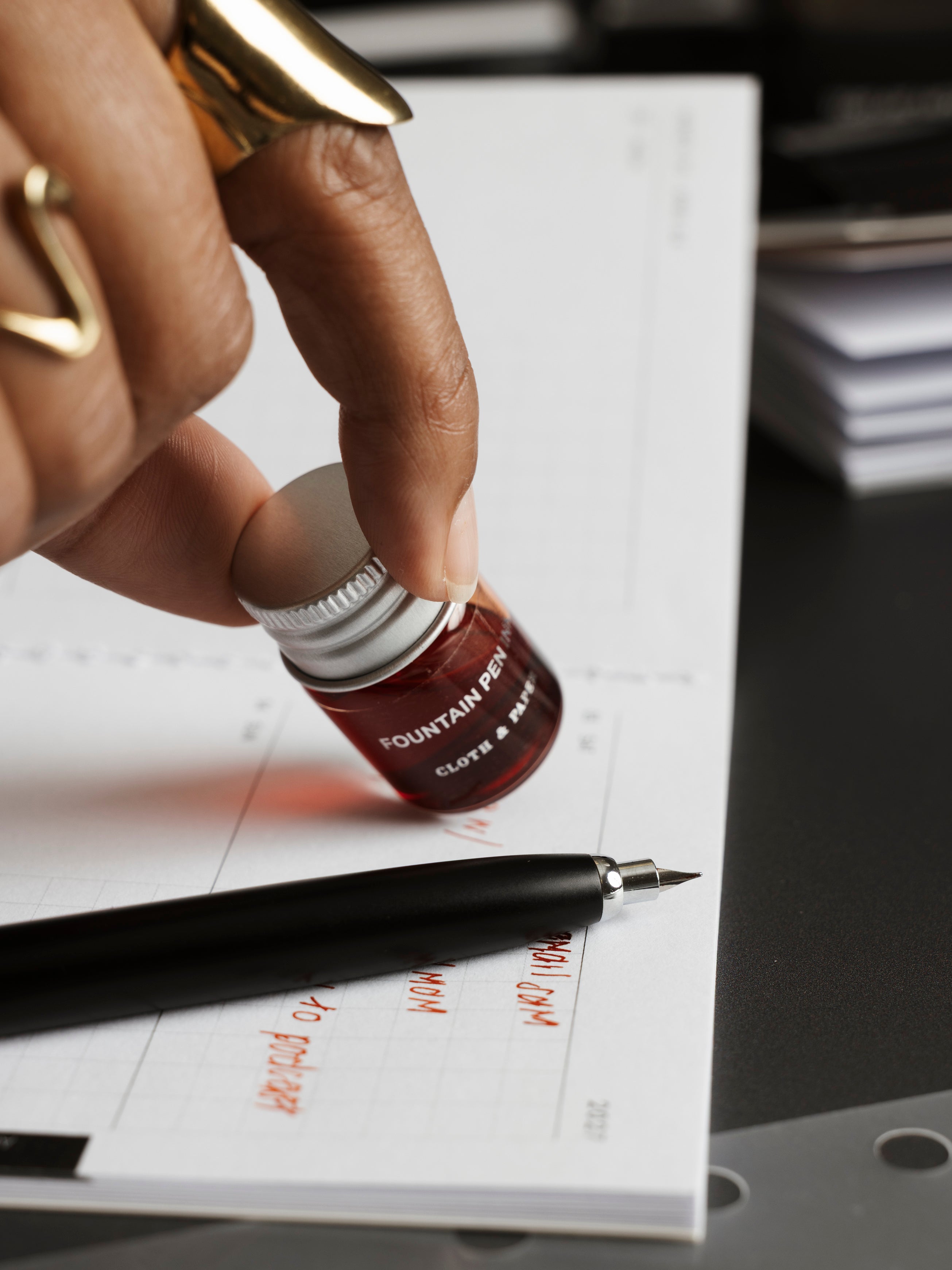 Mini Fountain Pen Ink in Saffron, 5 mL clear glass bottle held beside a Lanbitou fountain pen resting on open planner pages with orange handwriting