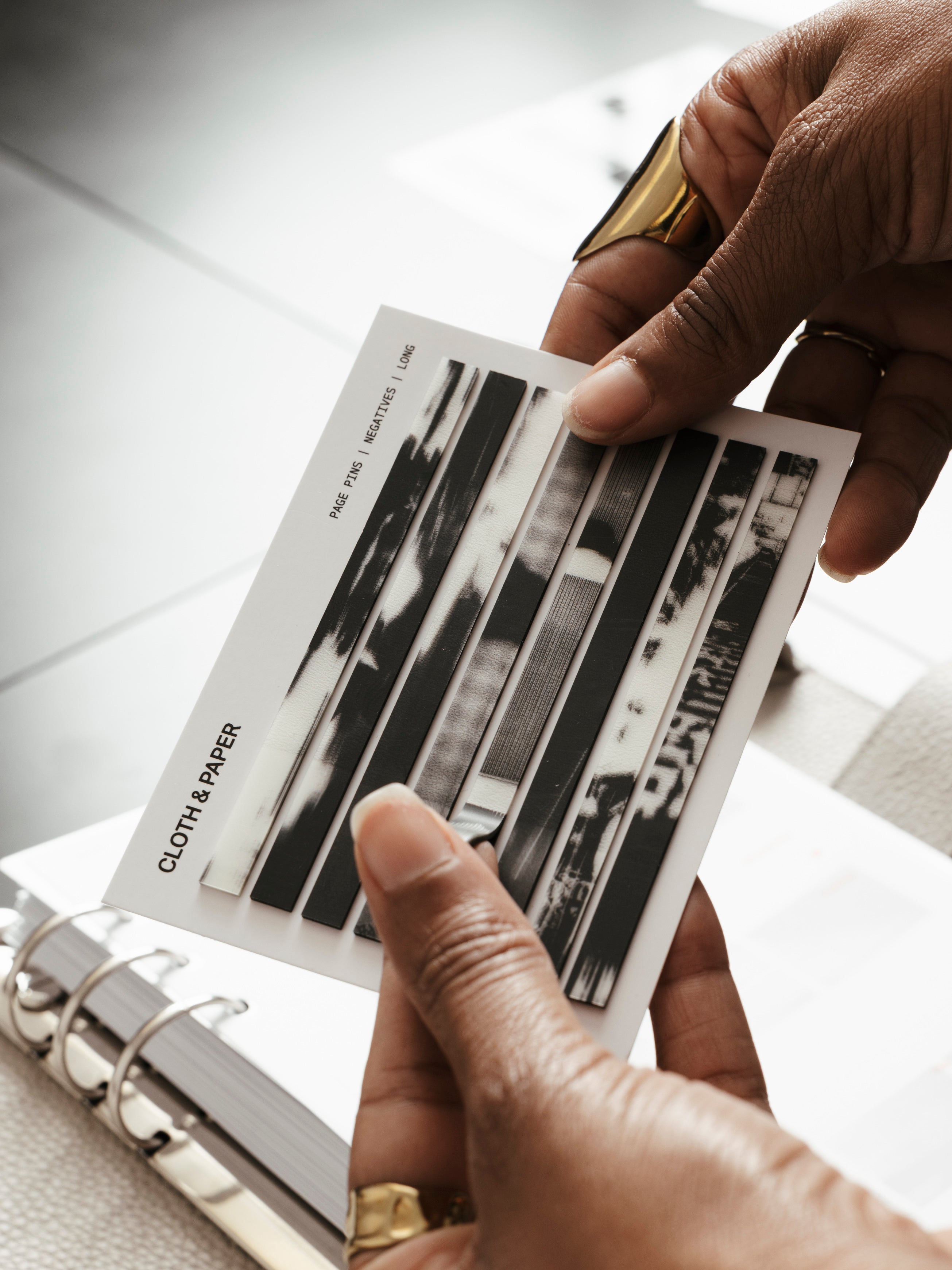 Page Pins | Long | Negatives, woman holding full set of 160 transparent grey-toned film negative-style page pins on a white backing card