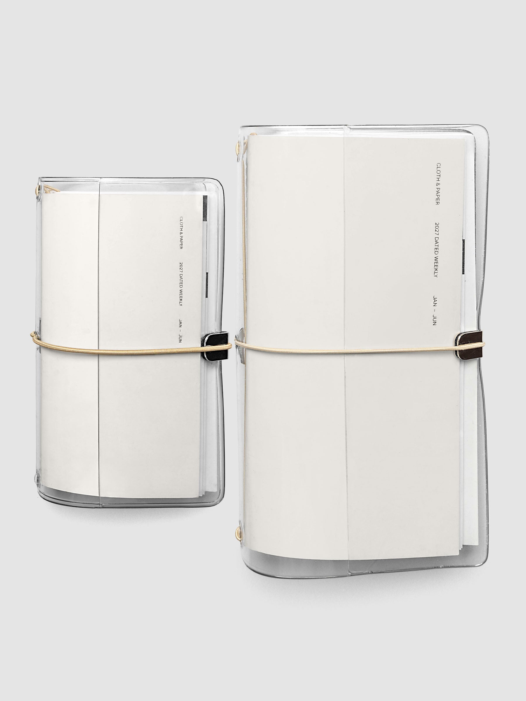 Two closed travel notebooks side by side in clear vinyl covers with tan bungee cords, both reading 2027 Dated Weekly January through June, comparing Pocket Plus and A5 Slim sizes