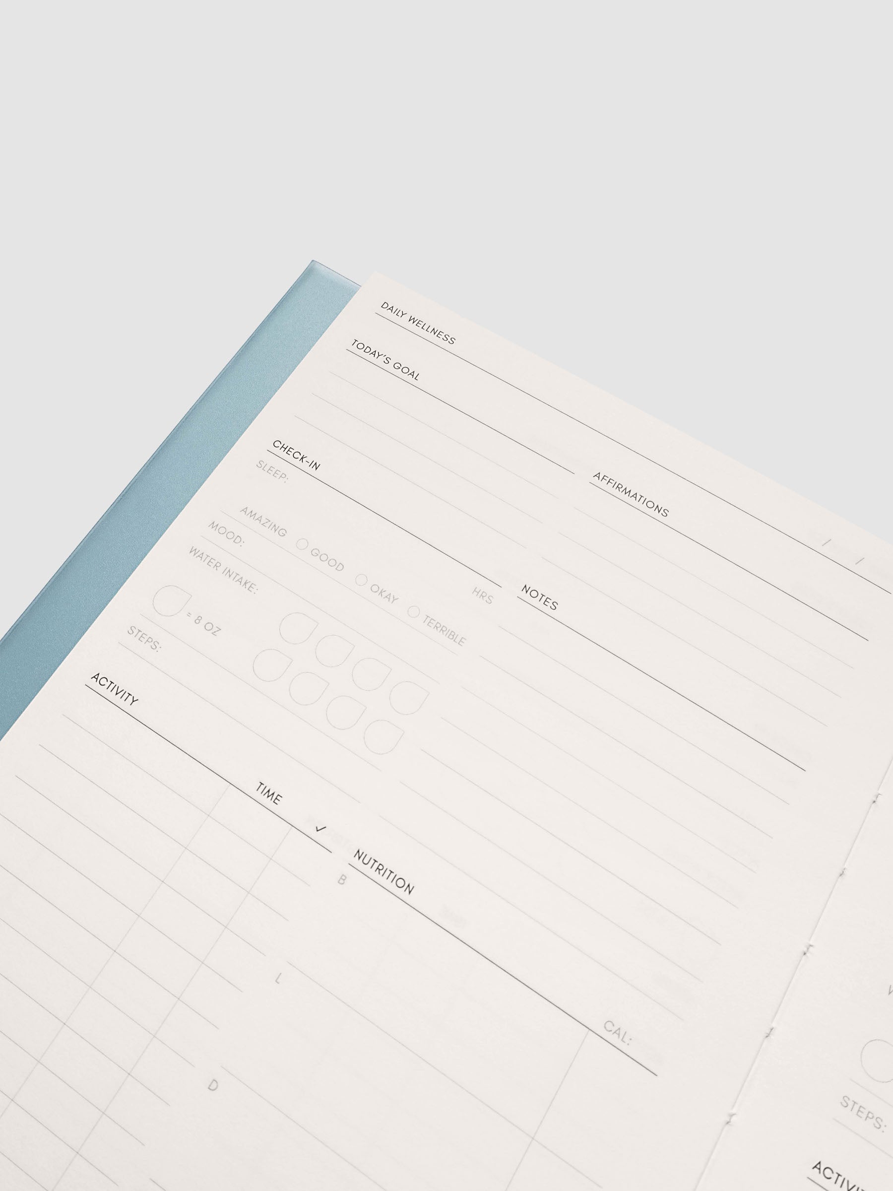Close up of the Perfect Bound Notebook | A5 | Daily Wellness open at an angle, light blue spine edge beside a ruled column layout