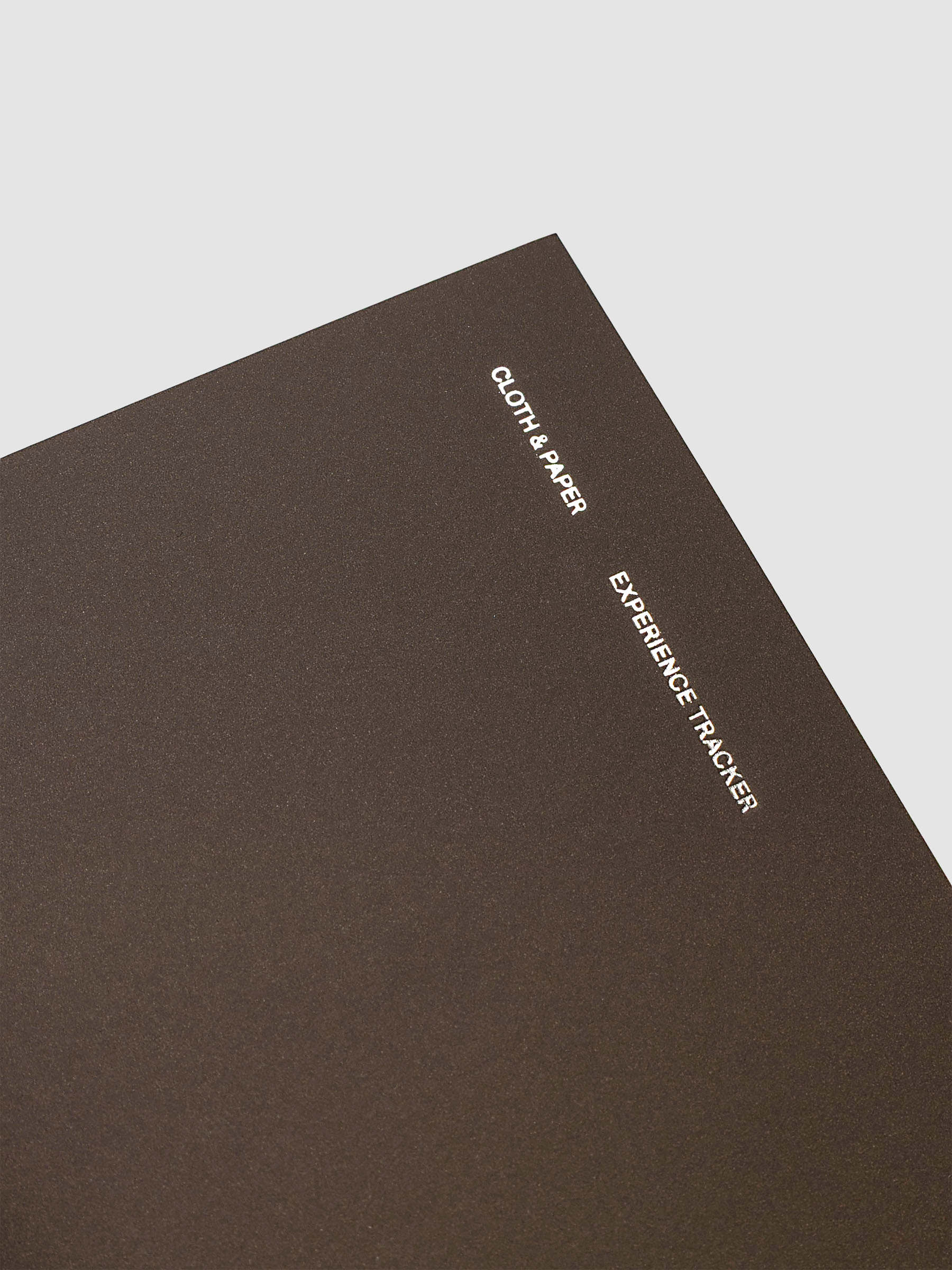 Close up of the Experience Tracker Pocket Plus travel notebook in Walnut with gold foil cover text, displayed on a neutral background