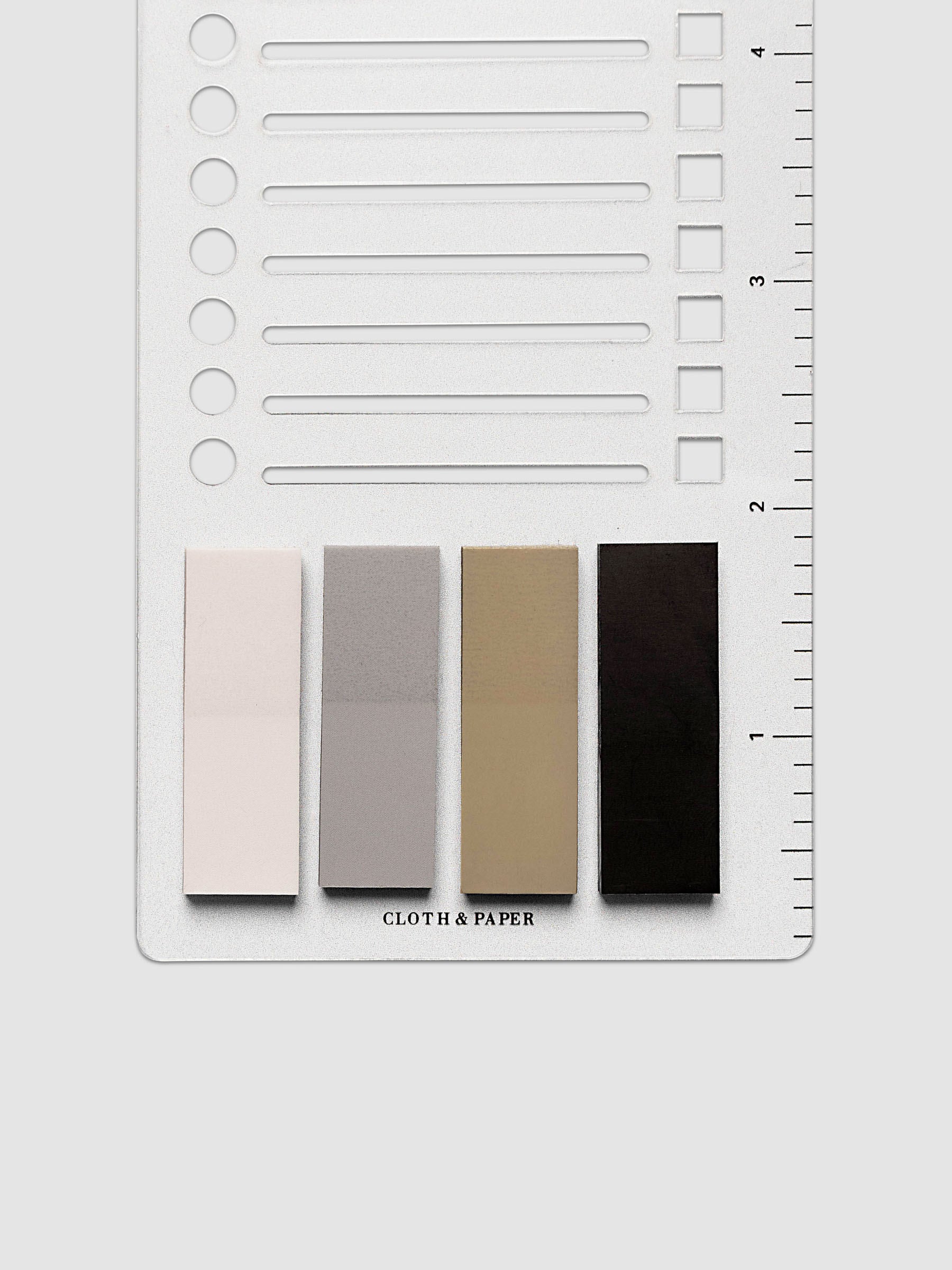 Stencil Page Flag Set, close-up of lower half of clear plastic stencil showing cutout lines, circles, and squares with ruled edge, and four page flag colors below: blush pink, light gray, warm tan, and near-black