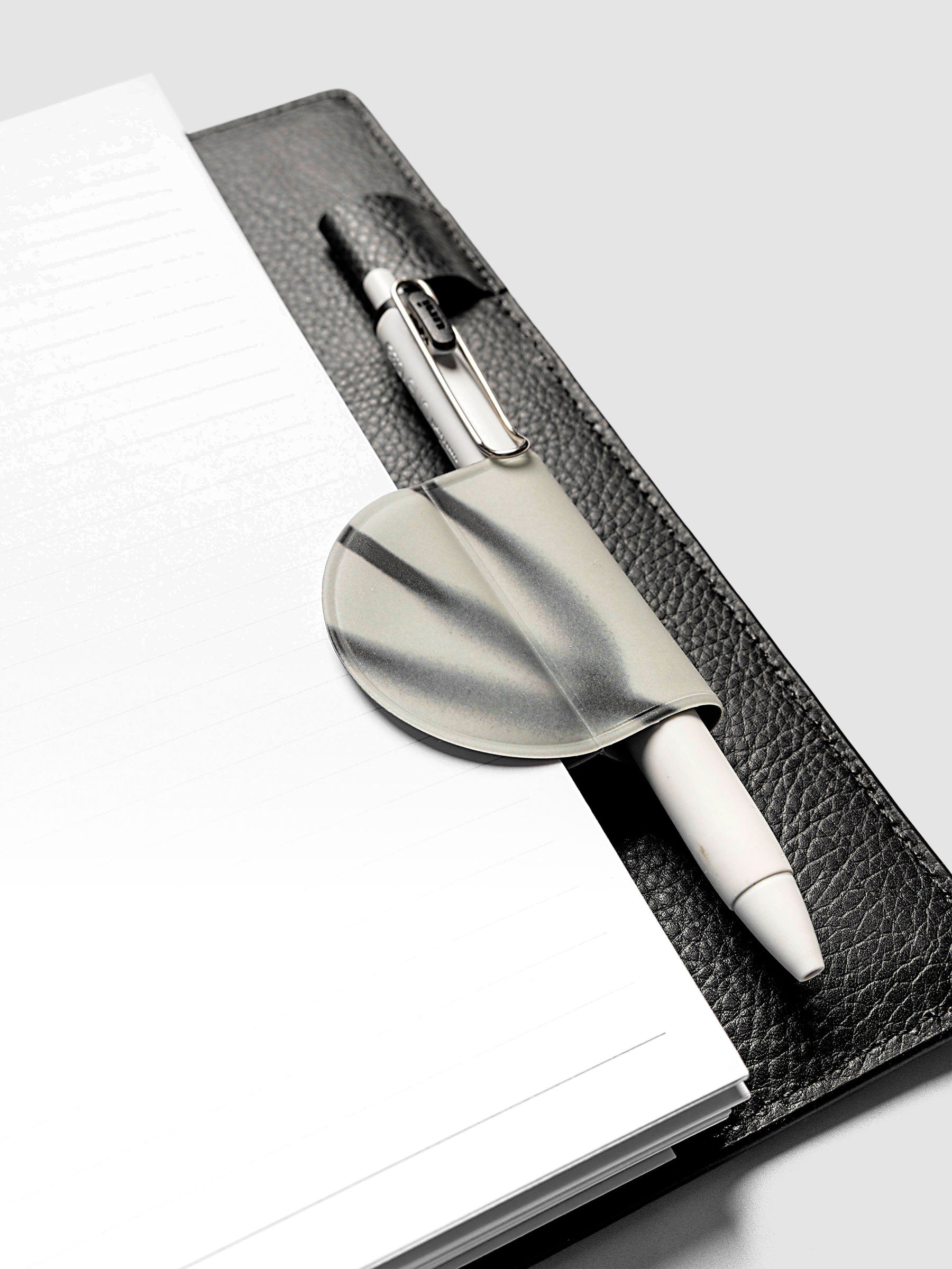 Magnetic Bookmark | Pen Holder | Vinyl in Blurred Line holding a white pen, clipped to the spine of an open black leather planner