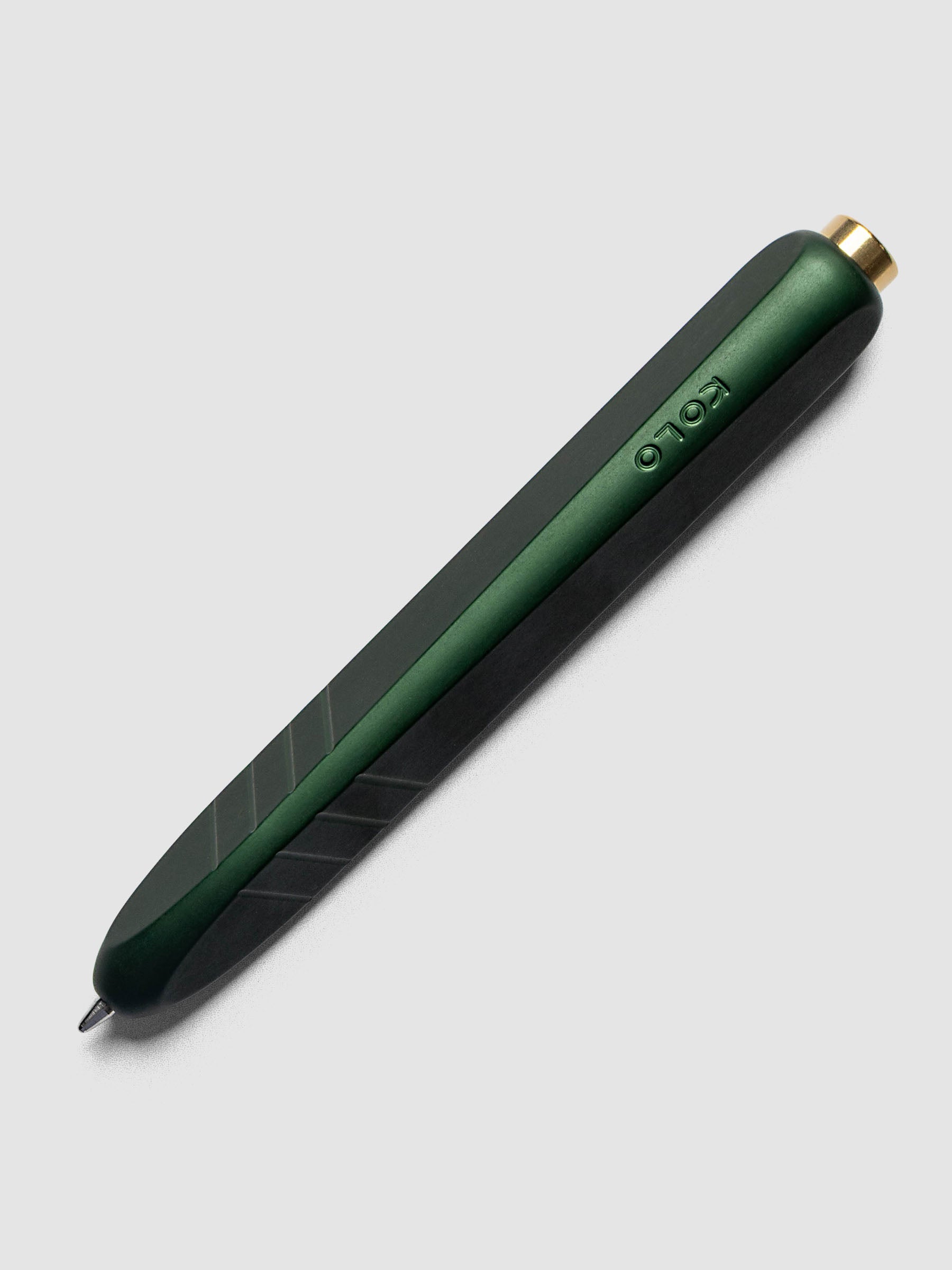 Kolo Tino Ballpoint Pen in Anodized Aluminum Verdant, a deep forest green barrel with gold top button, tip extended, angled view