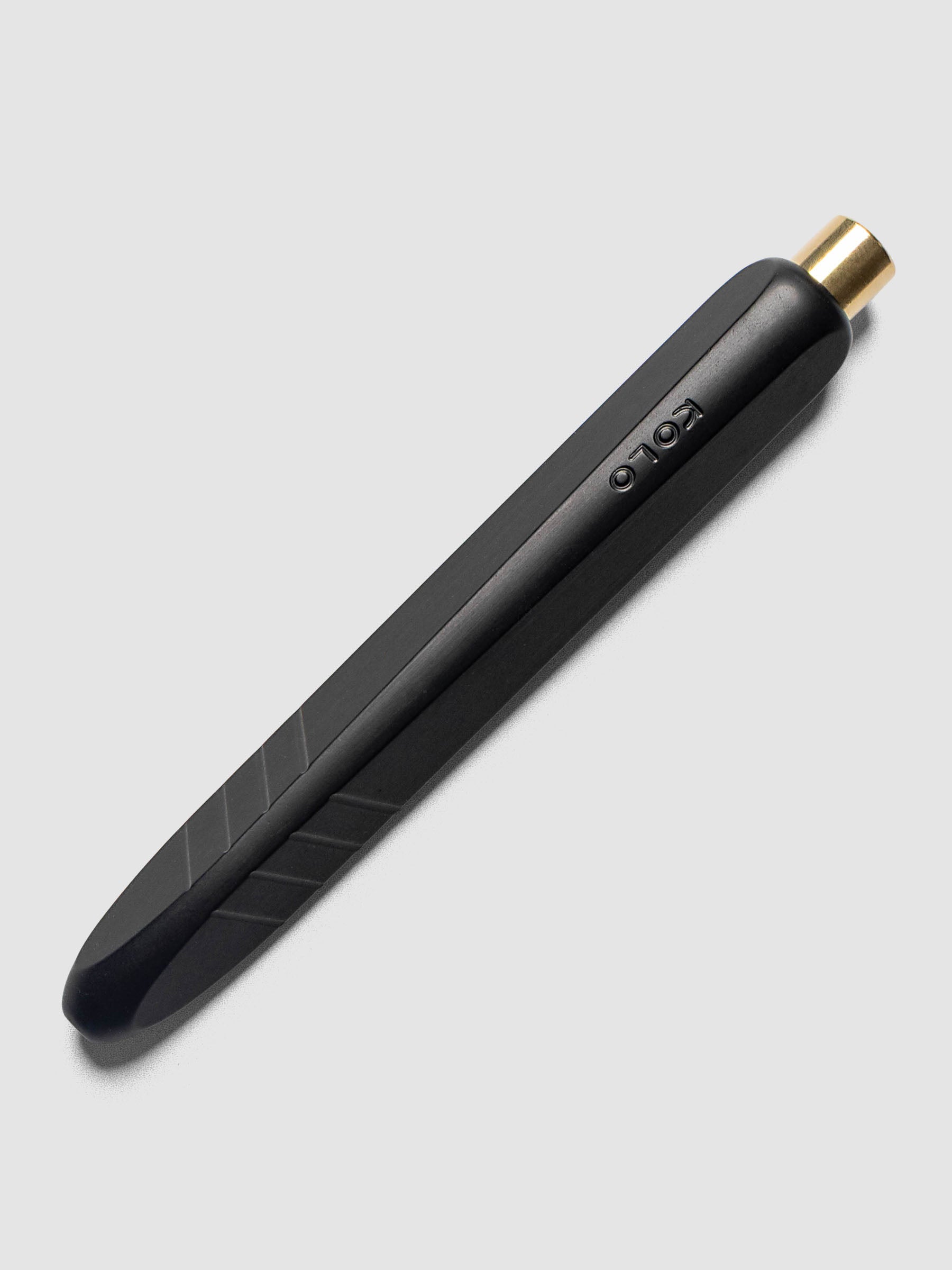 Kolo Tino Ballpoint Pen in Anodized Aluminum Noir, a matte black barrel with gold top button, retracted, angled view