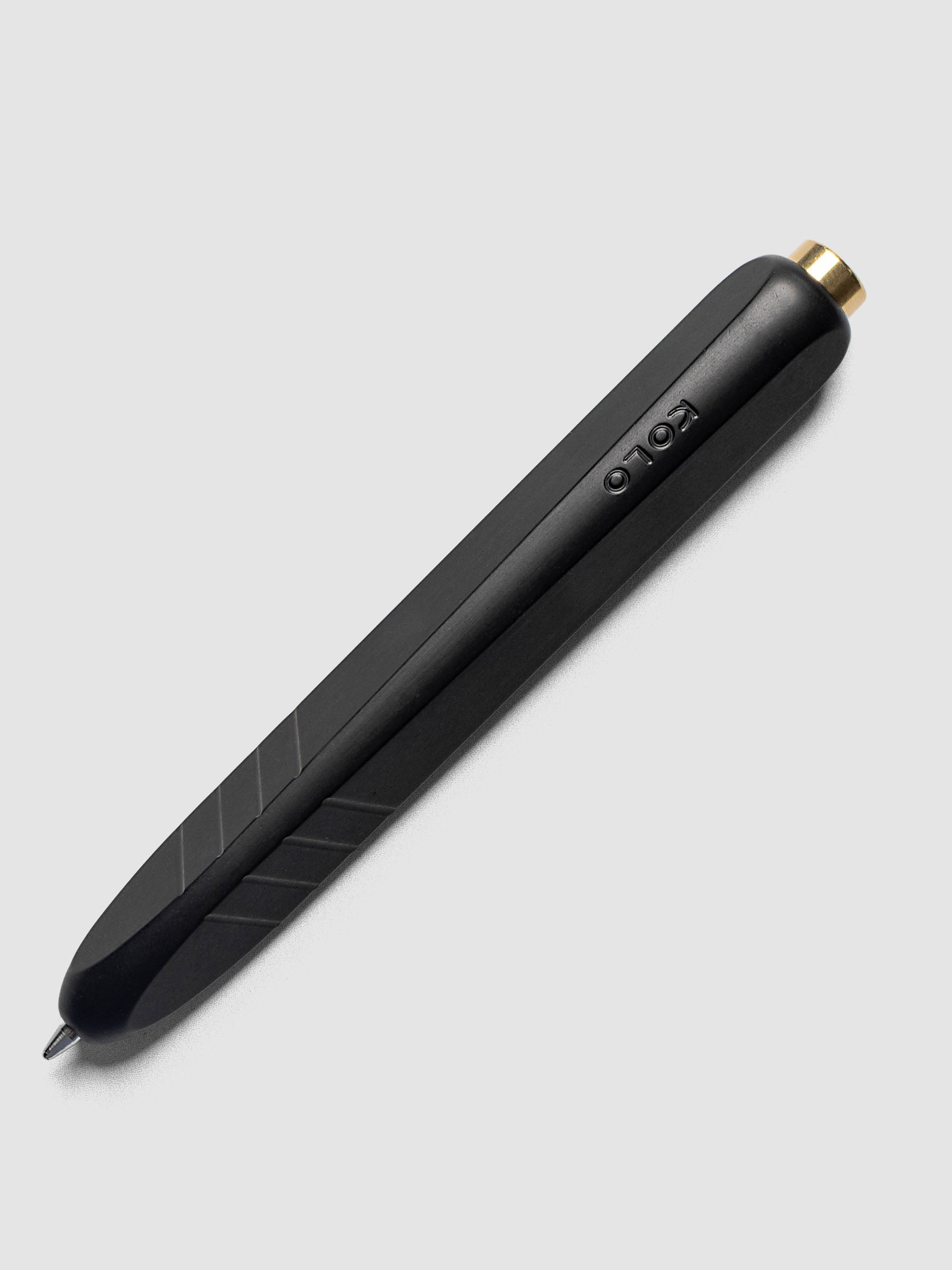 Kolo Tino Ballpoint Pen in Anodized Aluminum Noir, a matte black barrel with gold top button, tip extended, angled view