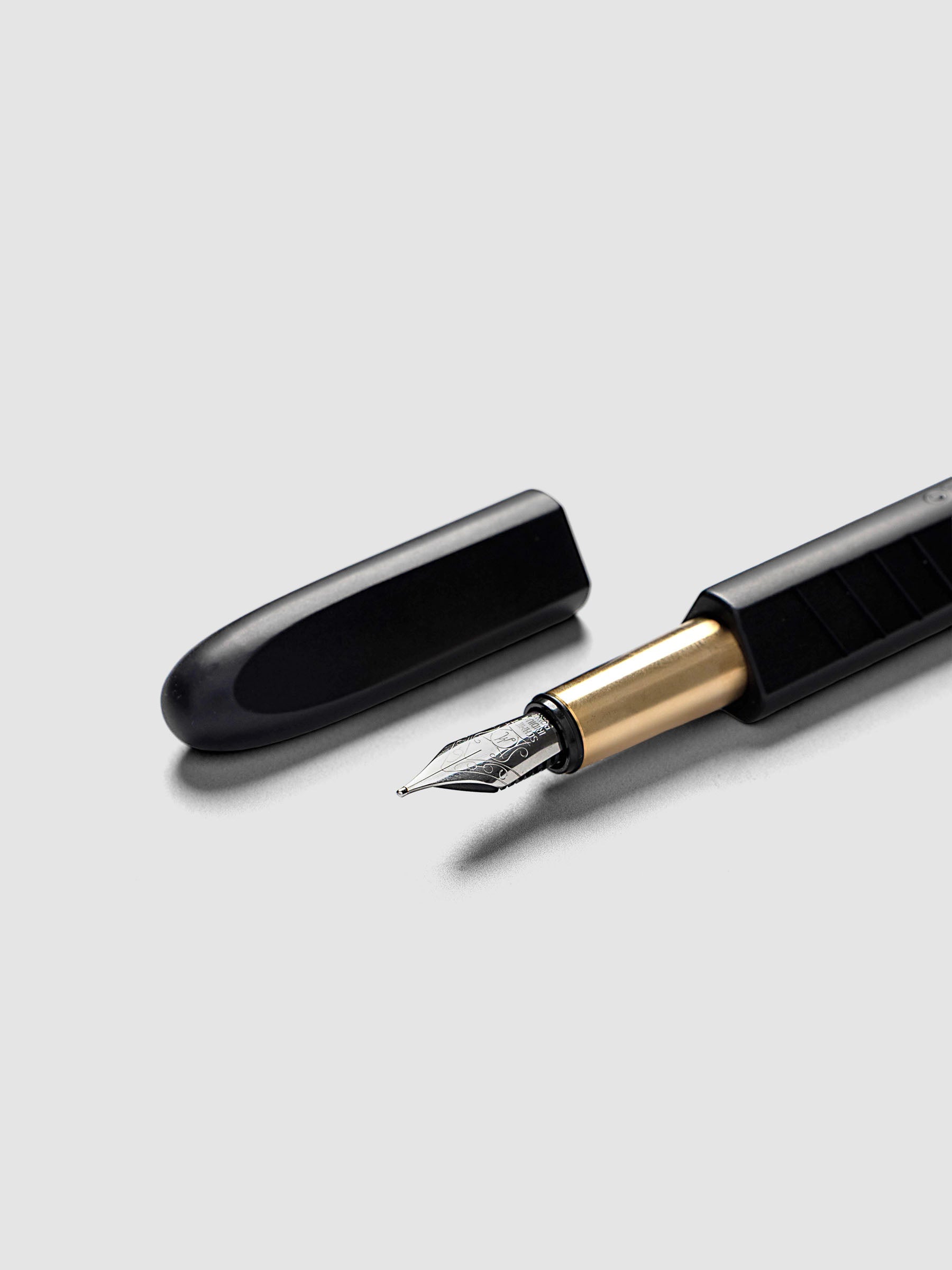 Kolo Tino Fountain Pen in Anodized Aluminum Noir, a matte black barrel with gold accents and silver medium nib shown with cap off, close-up