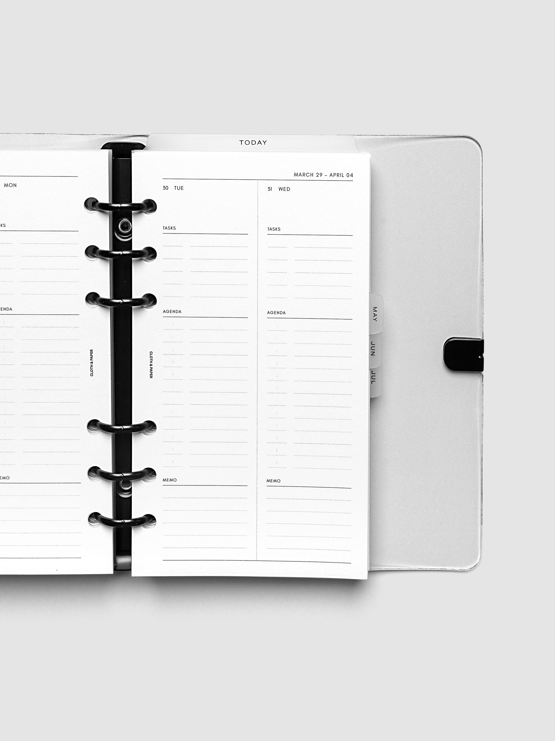 Close-up of an open planner with black 6-ring binding, weekly spread showing Tuesday and Wednesday daily columns with tasks, agenda, and memo sections, tabbed monthly dividers visible at the edge, Personal 6-Ring Punch size