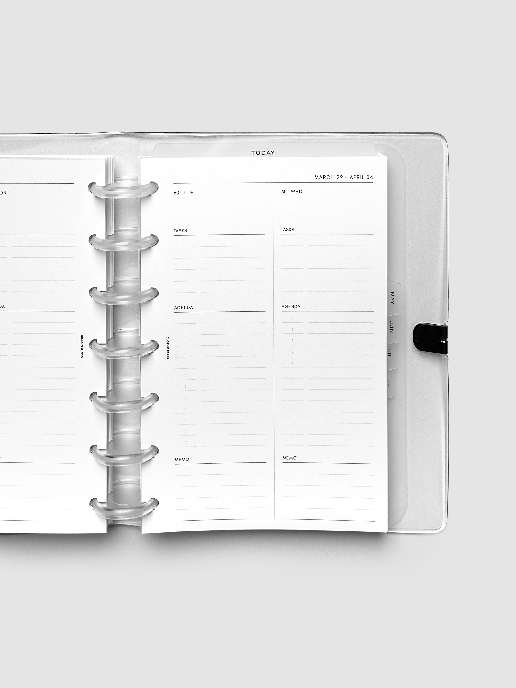 Close-up of an open planner with clear 7-disc binding, weekly spread showing Tuesday and Wednesday daily columns with tasks, agenda, and memo sections, tabbed monthly dividers visible at the edge, HP Mini 7-Disc Punch size
