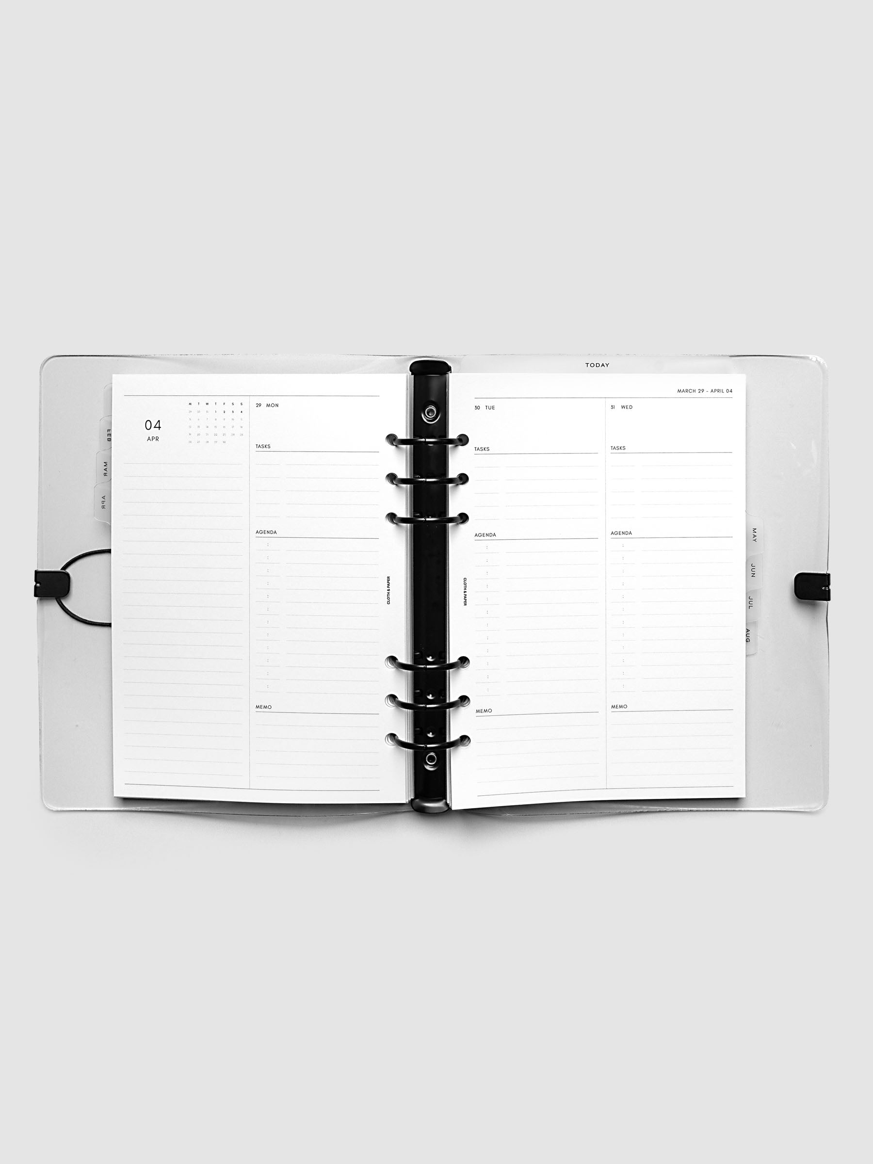 Flat lay of an open planner with black 6-ring binding at the center, a Monday through Wednesday spread across two facing pages with a mini monthly calendar, daily tasks, agenda, and memo sections, A5 6-Ring Punch size