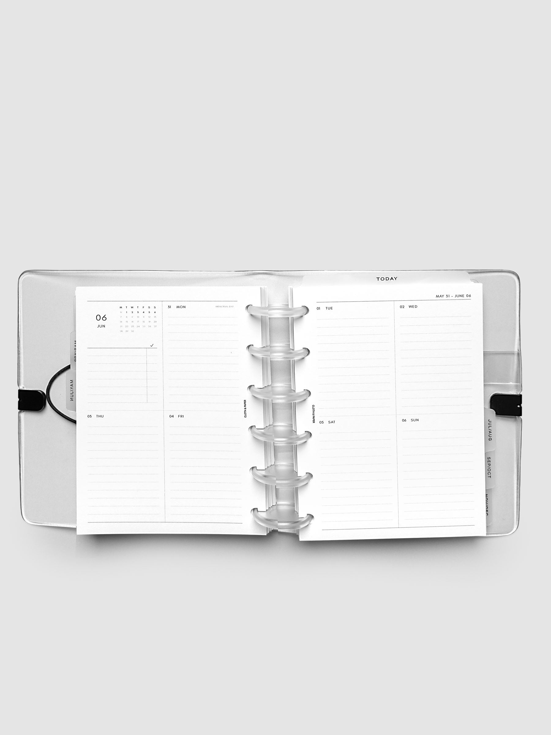 Flat lay of an open planner with clear 6-disc binding at the center, a Monday through Sunday weekly vertical spread across two facing pages with a mini calendar and lined daily sections, CP Petite 6-Disc Punch size