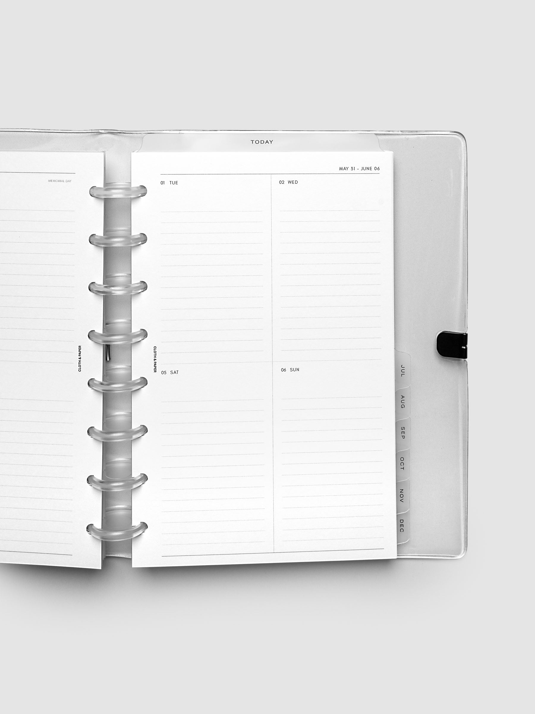 Close-up of an open planner with clear 8-disc binding, weekly vertical spread showing Tuesday through Sunday in a two-column grid with lined daily sections, tabbed monthly dividers visible at the edge, Half Letter 8-Disc Punch size