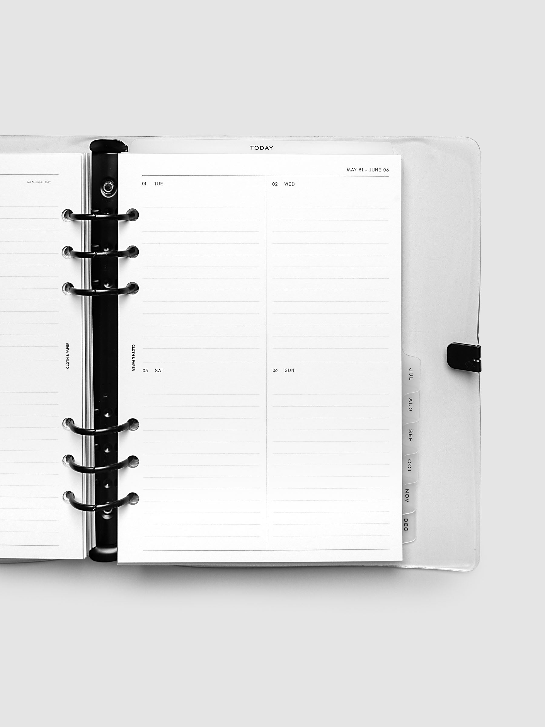 Close-up of an open planner with black 6-ring binding, weekly vertical spread showing Tuesday through Sunday in a two-column grid with lined daily sections, tabbed monthly dividers visible at the edge, A5 6-Ring Punch size