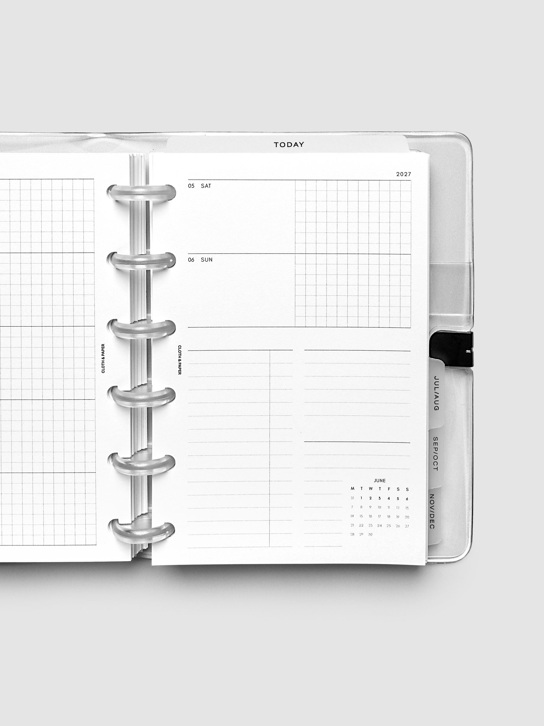 Close-up of an open planner with clear 6-disc binding, weekly horizontal spread showing Saturday and Sunday in a shared row split into lined and graph columns, tabbed monthly dividers visible at the edge, CP Petite 6-Disc Punch size