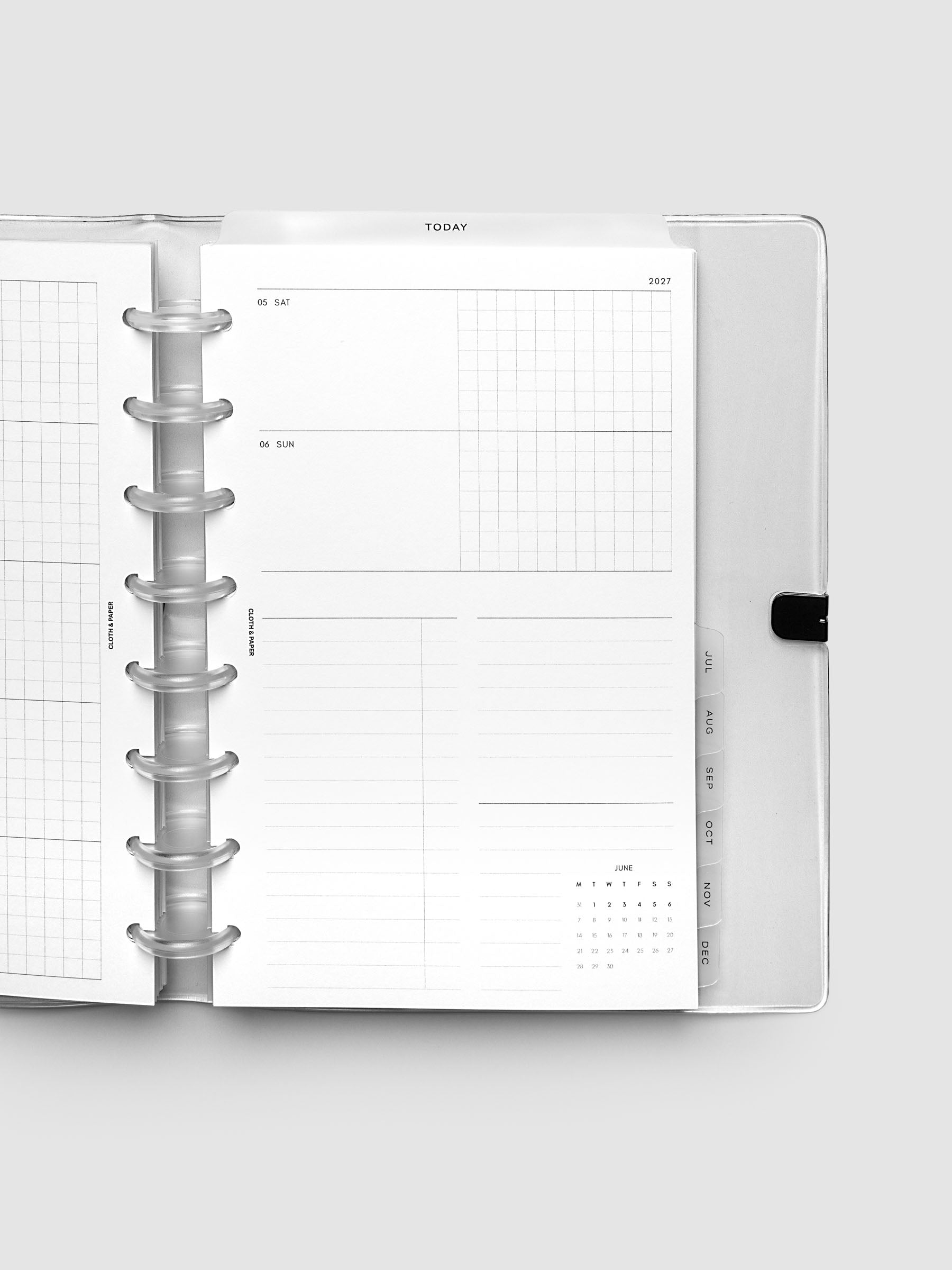 Close-up of an open planner with clear 8-disc binding, weekly horizontal spread showing Saturday and Sunday in a shared row split into lined and graph columns, tabbed monthly dividers visible at the edge, Half Letter 8-Disc Punch size